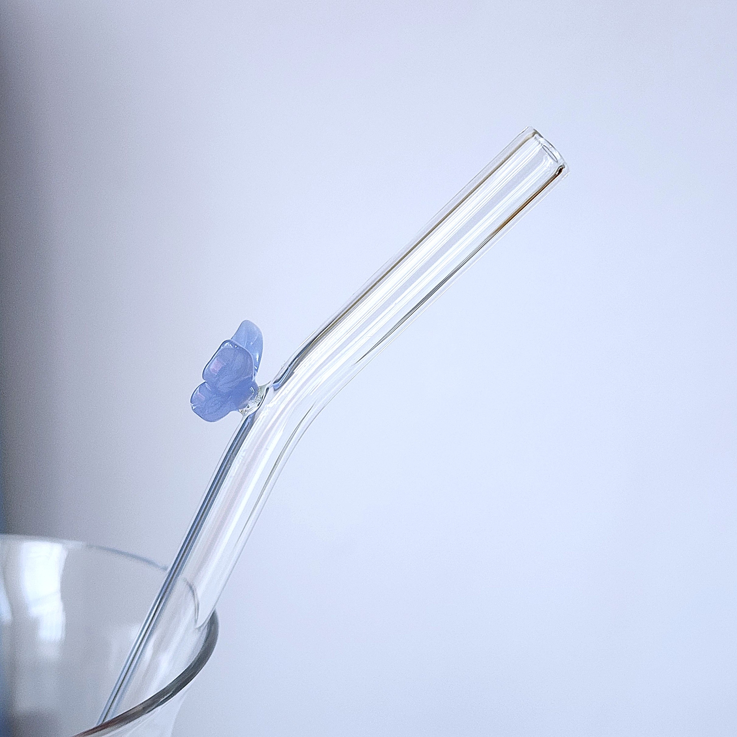 透明なガラス製のストローがカップに差し込まれている。ストローには青い蝶の装飾がある。