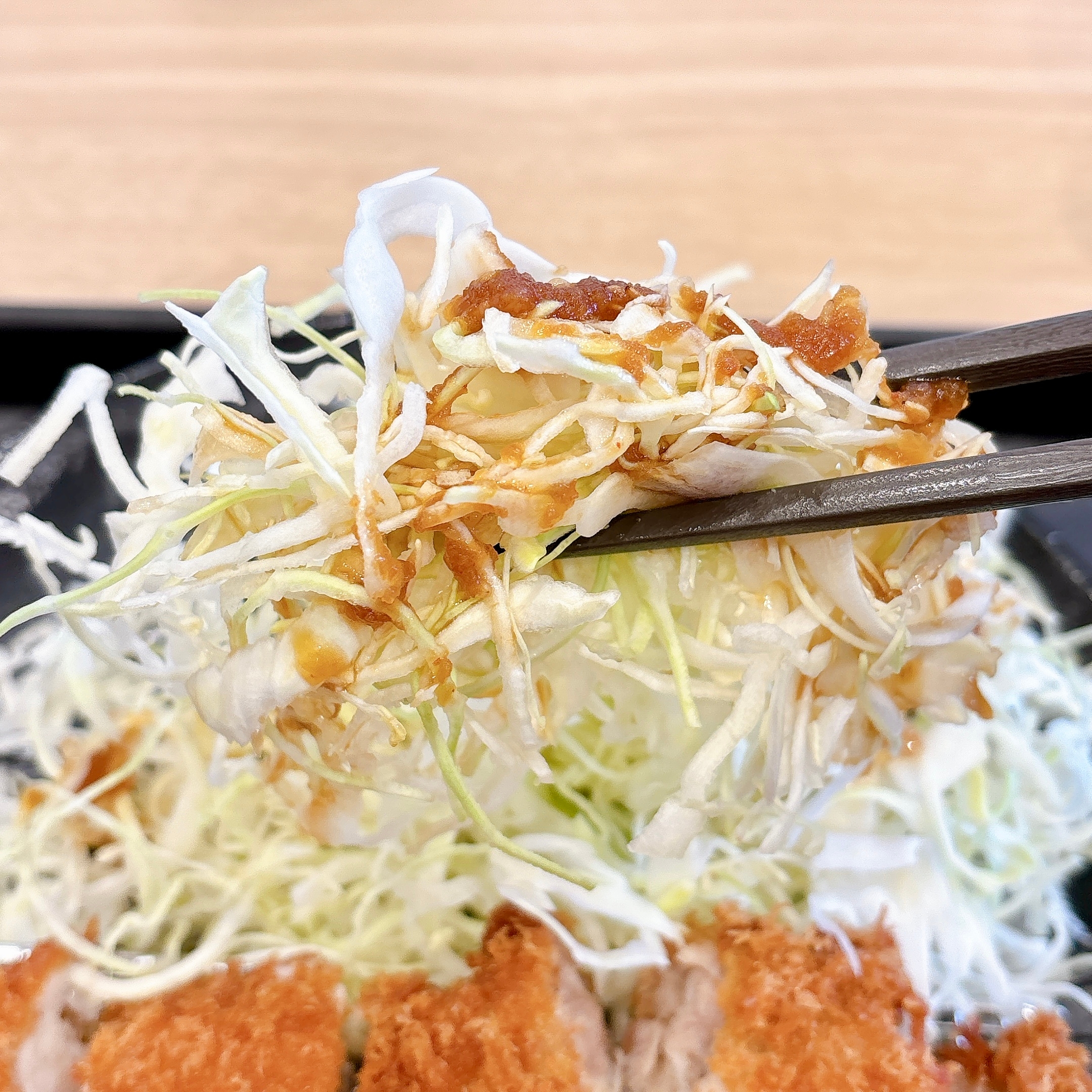 千切りキャベツを箸で持ち上げる、下には衣を付けた揚げ物が見える食事シーン。