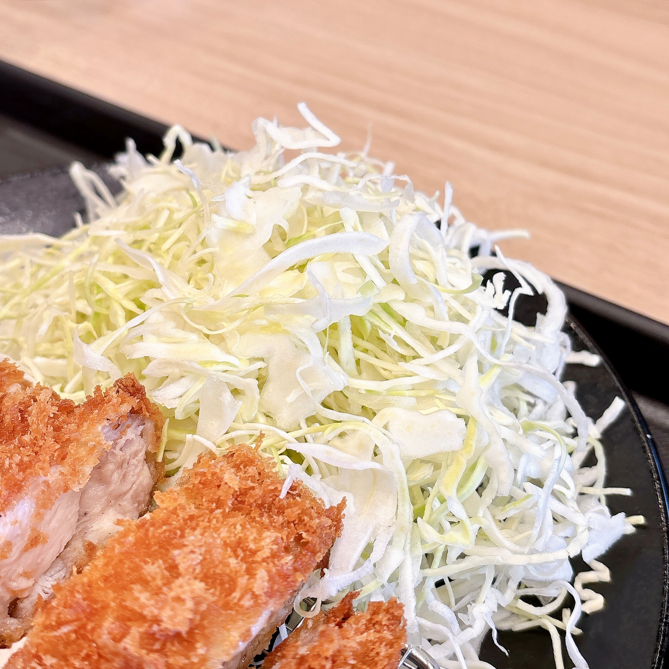 キャベツの千切りとトンカツが載った黒い皿。