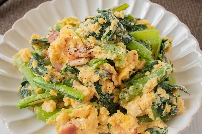 お皿に盛られた小松菜と卵の炒め物。ほうれん草やベーコンが混ざっています。