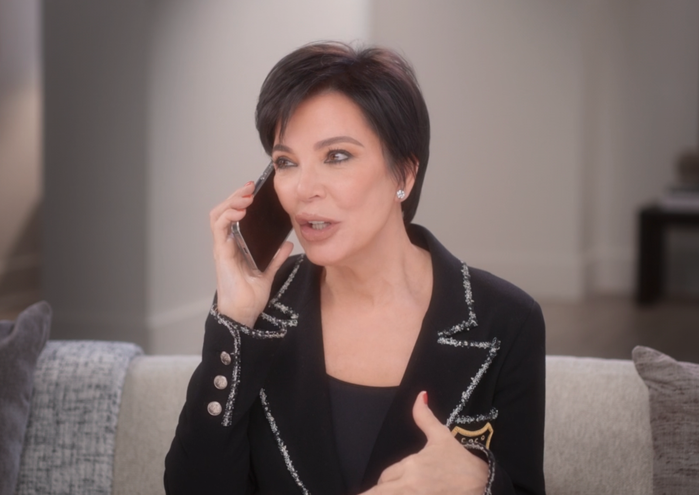 Kris Jenner talking animatedly on a phone while sitting on a sofa