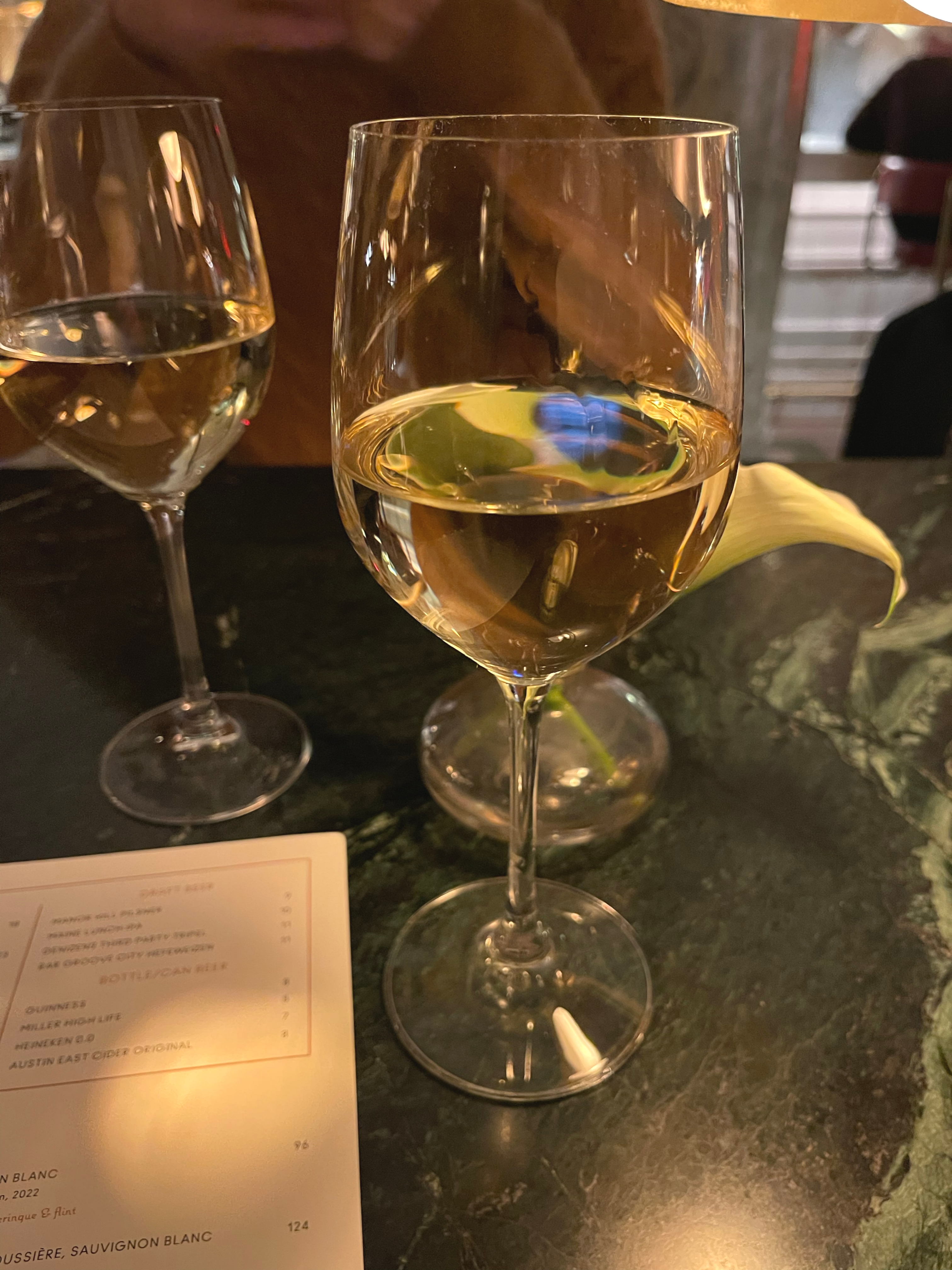 Two glasses of white wine on a table, beside a menu and a decorative calla lily