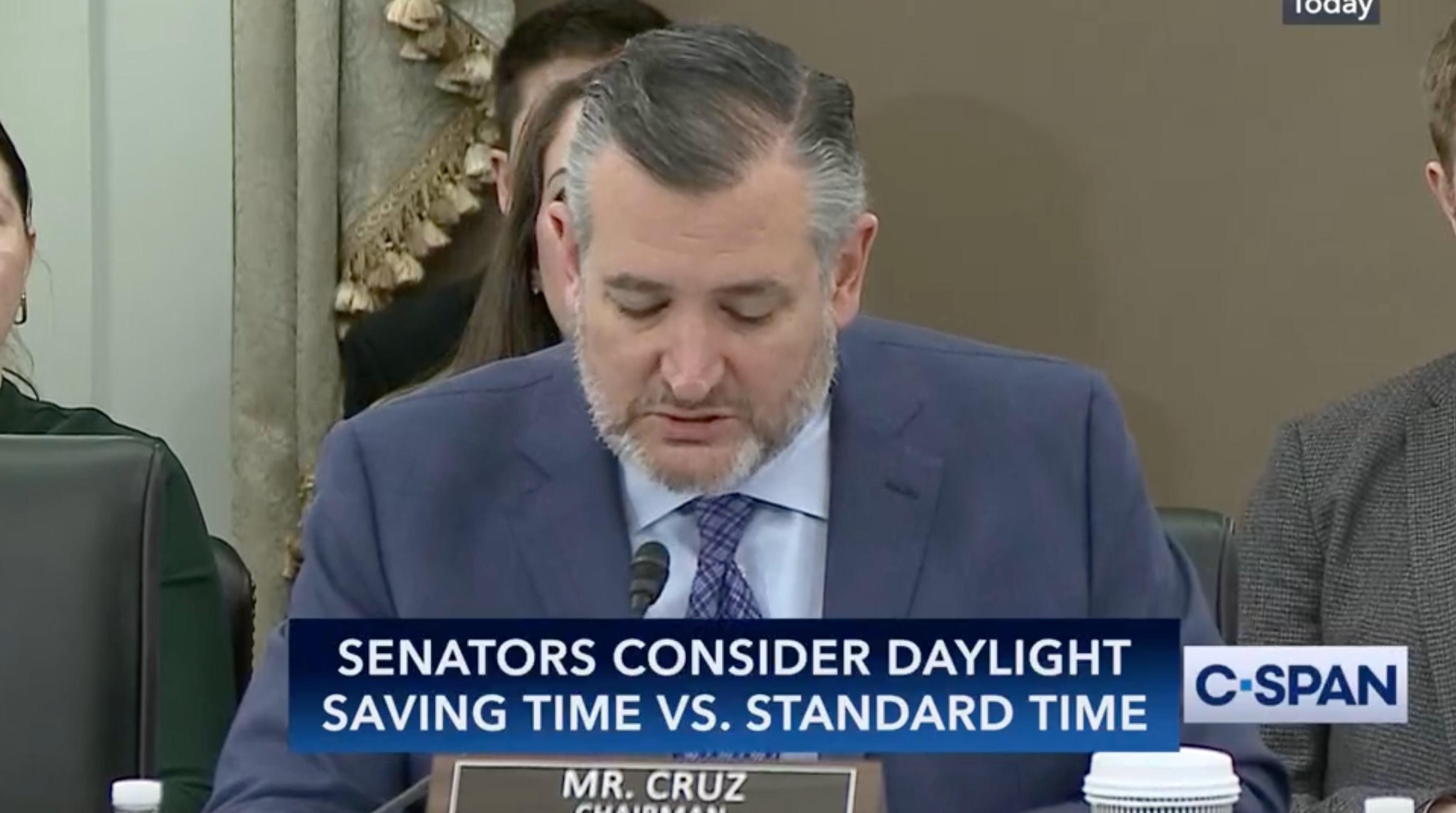 Senator at a meeting discussing daylight saving time versus standard time, with a C-SPAN banner displaying the topic