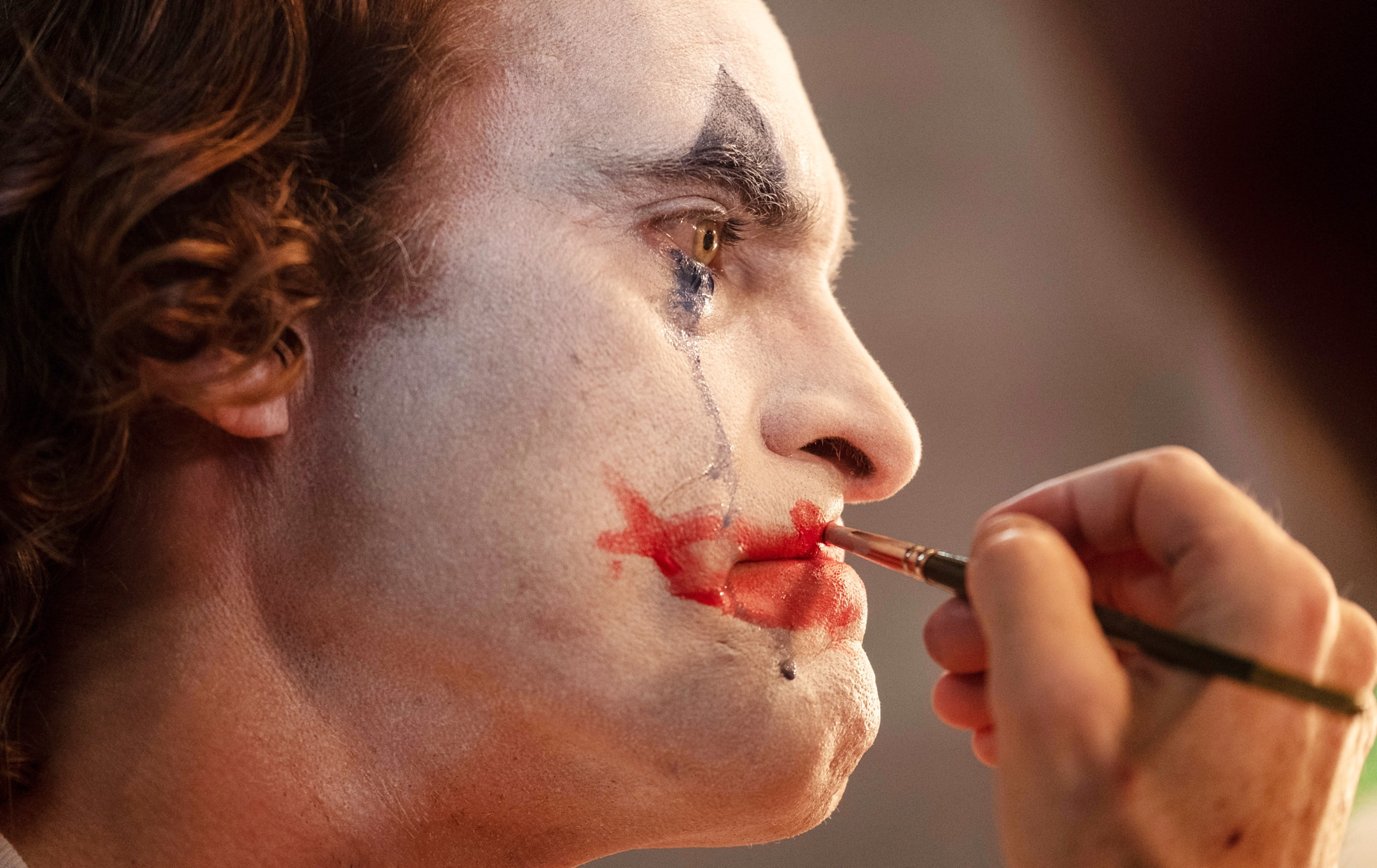 Person having clown makeup applied, focusing on exaggerated painted smile and eyes