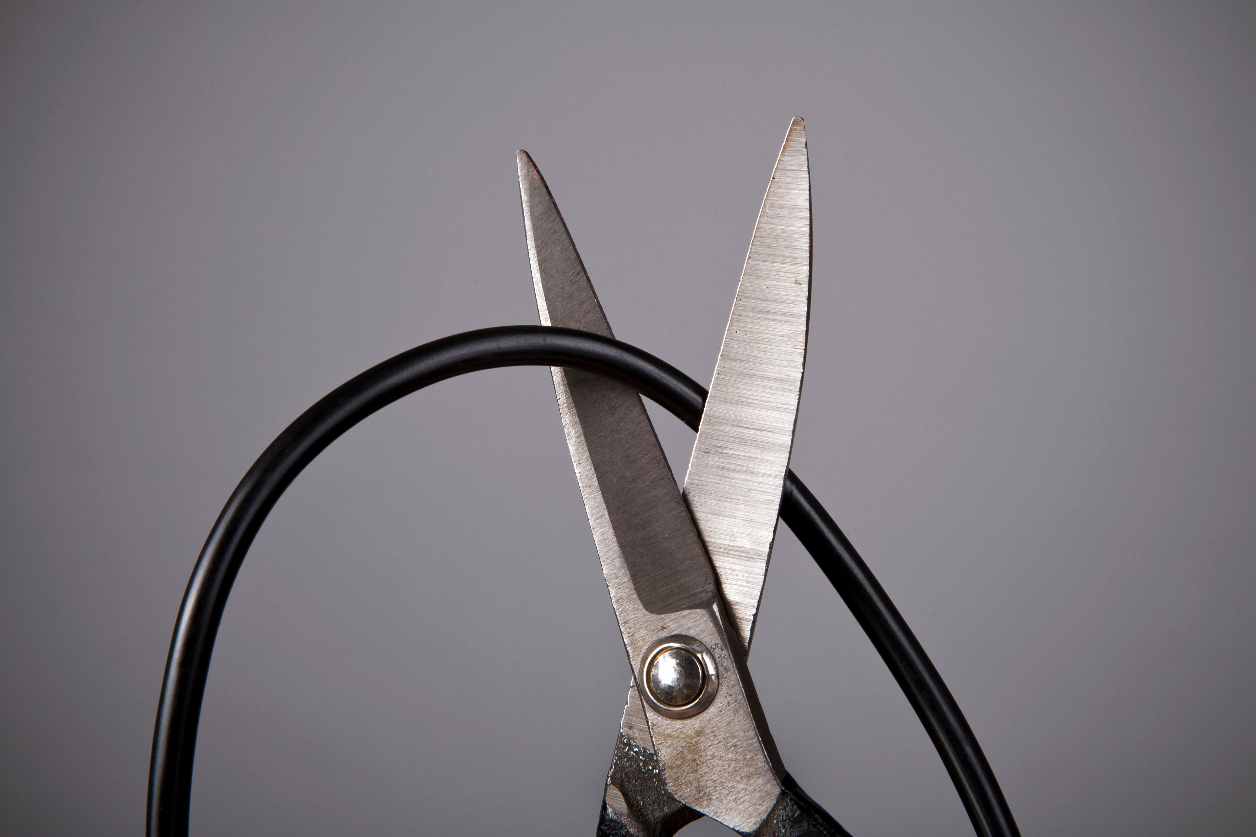 Scissors cutting a black cable against a plain background, symbolizing cutting off or disconnecting from something