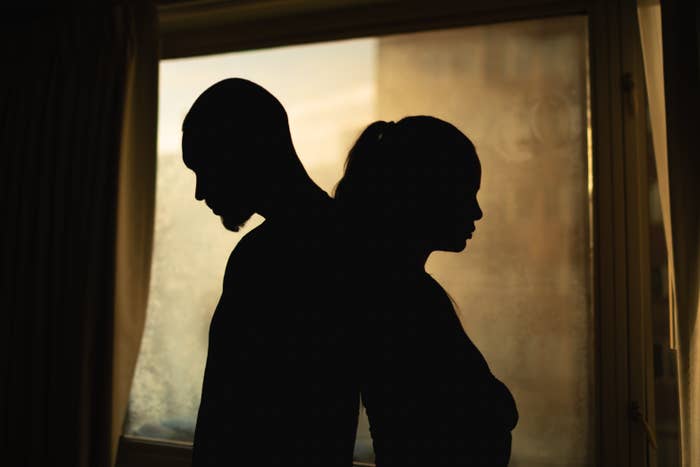 Two people in silhouette stand back-to-back near a window, creating a dramatic and introspective scene