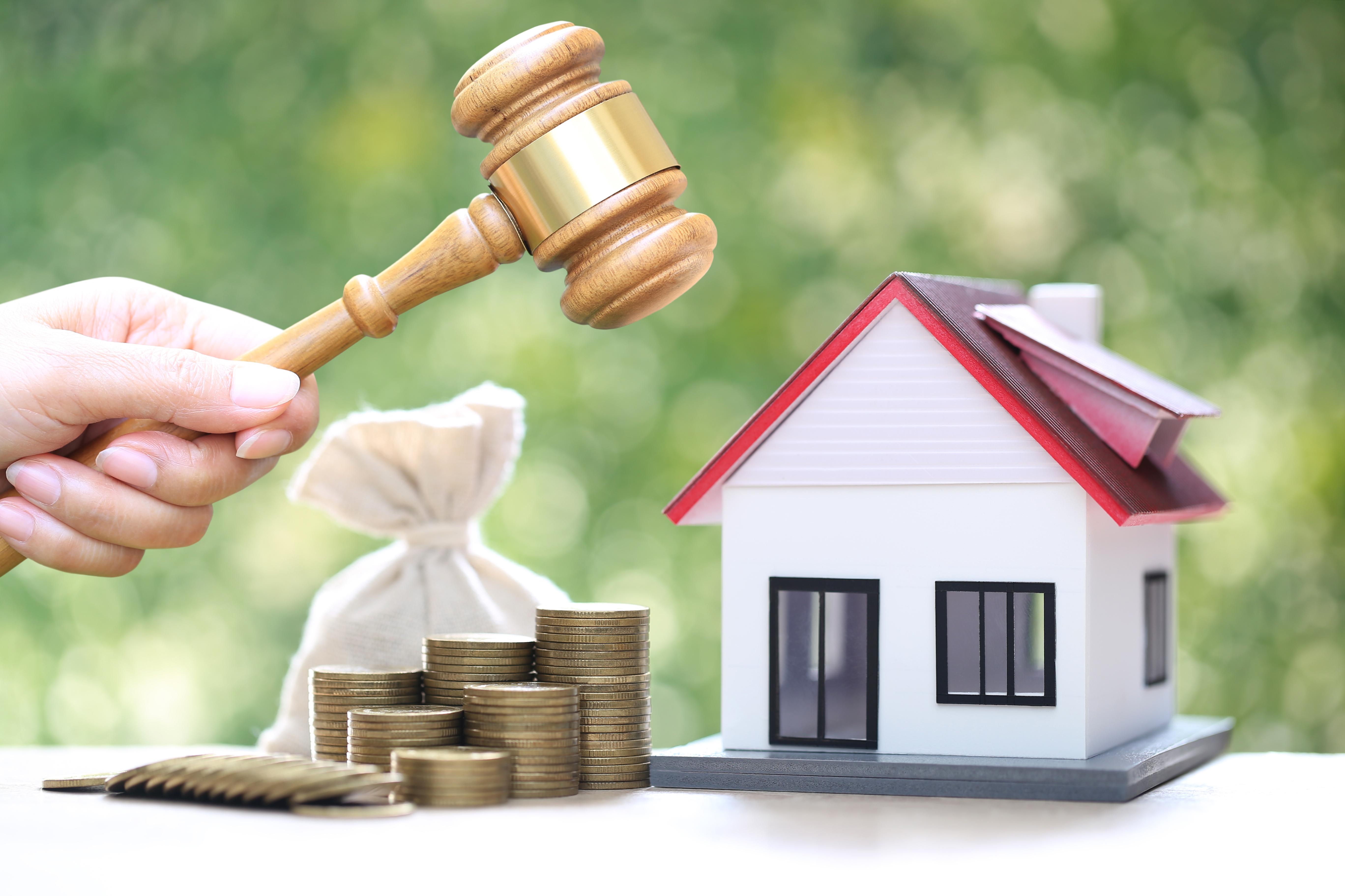 Gavel held beside a model house, stacked coins, and a money bag, symbolizing real estate or foreclosure