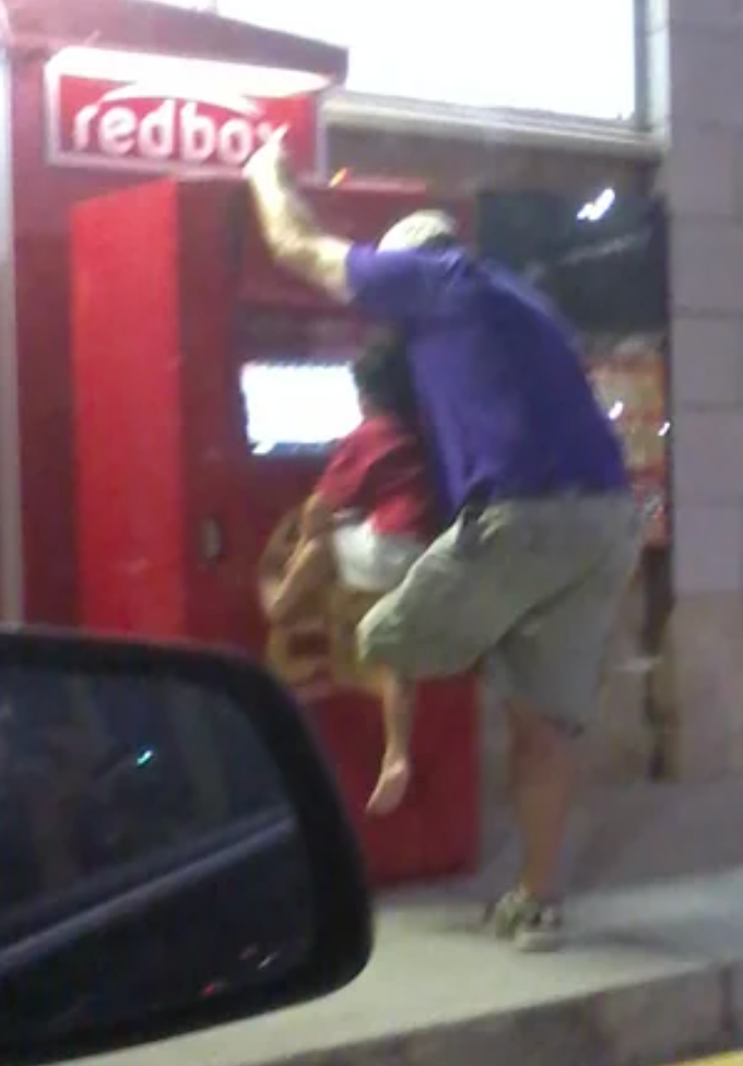Man using a child to reach a Redbox DVD rental machine for assistance