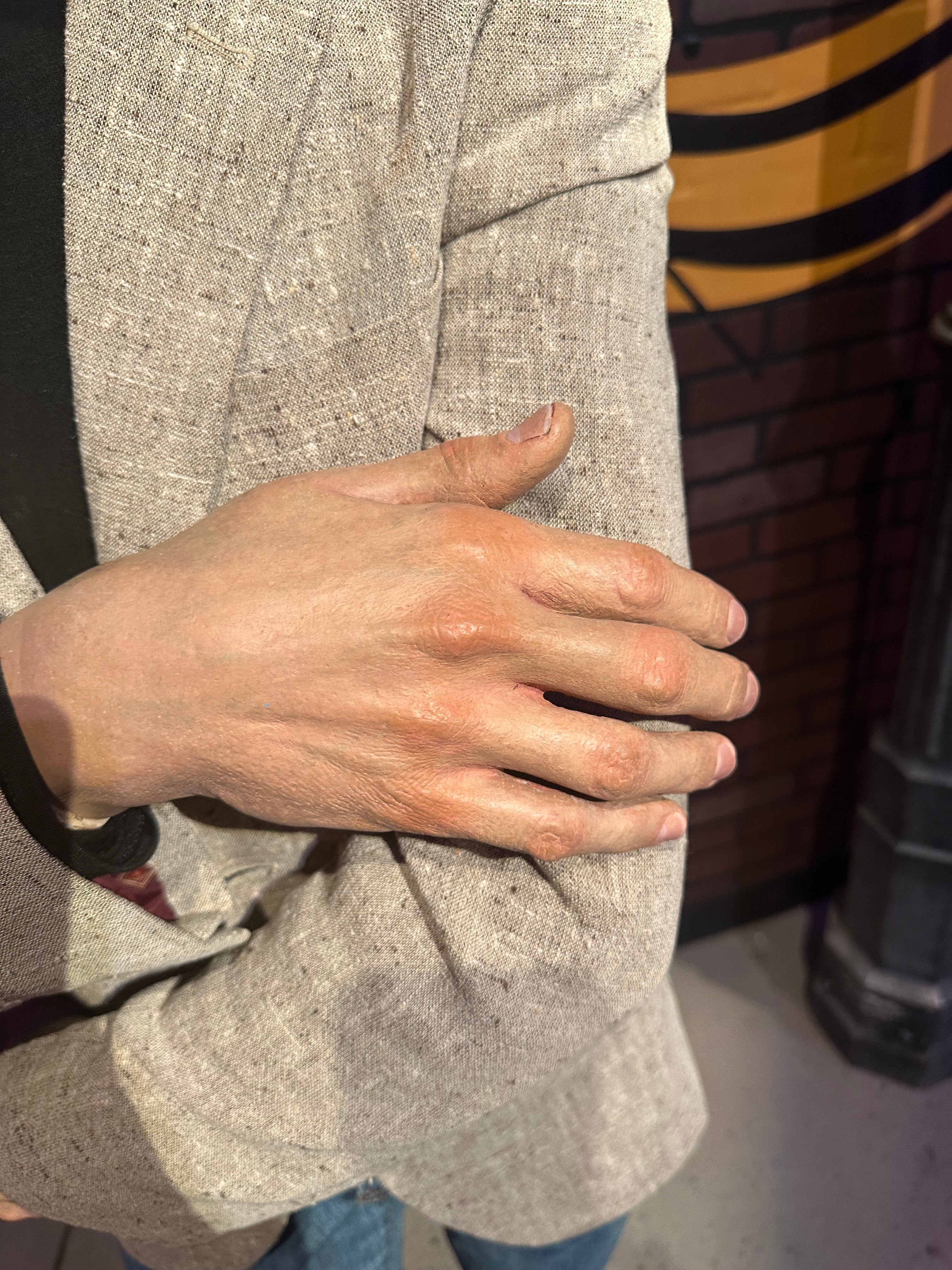 Person's hand on their own arm, wearing a textured blazer, standing by a brick wall