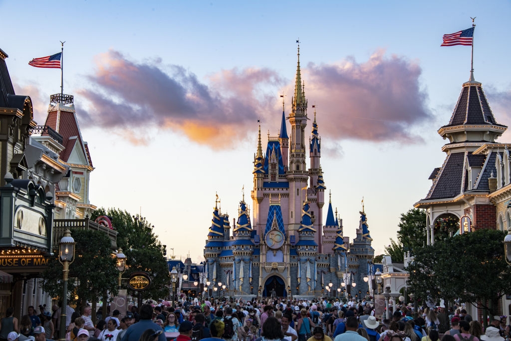 Crowd in front of a Disney castle, flags waving above, with people enjoying the lively theme park atmosphere at sunset