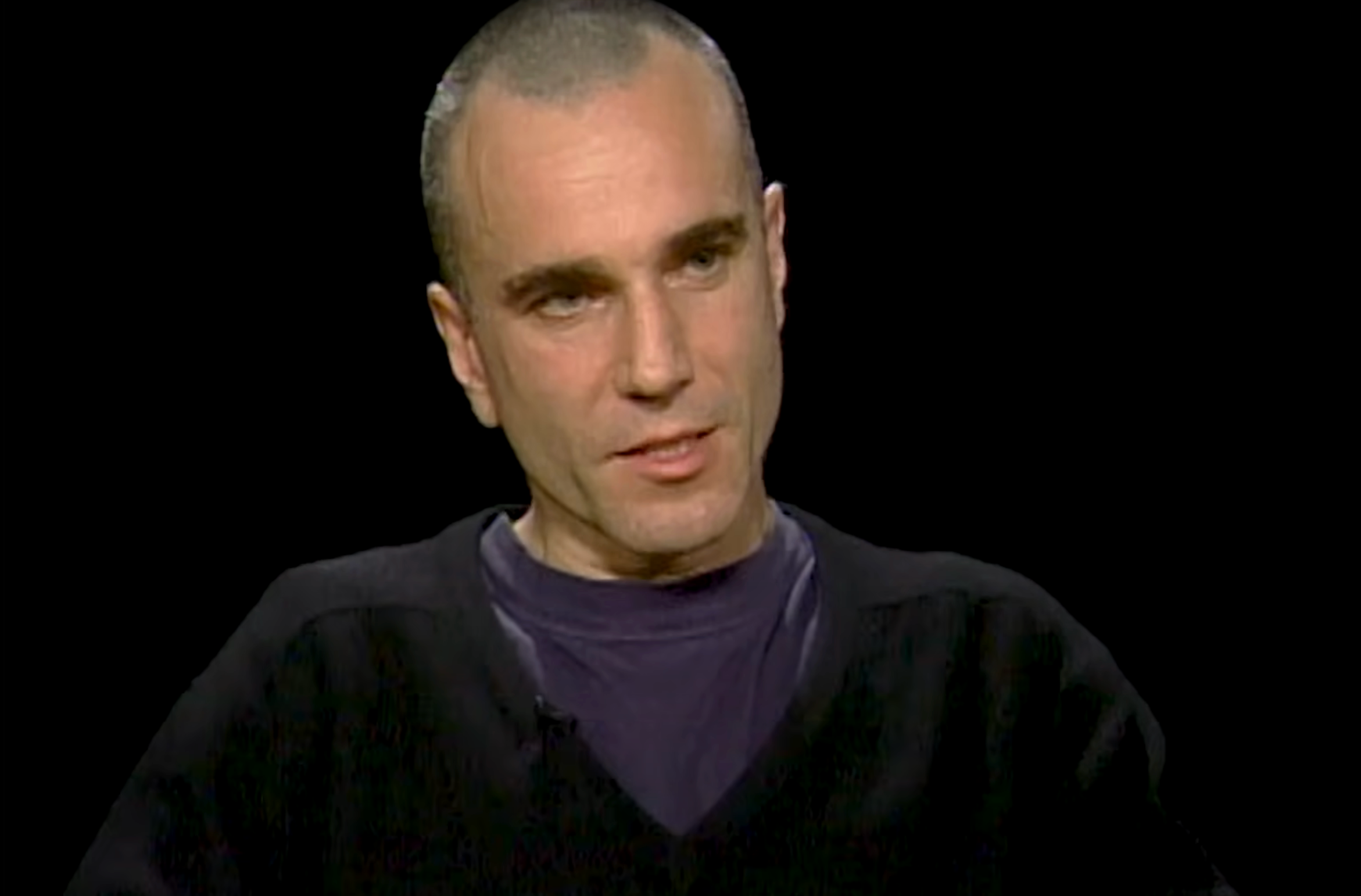 A person with short hair and a sweater on a dark background, speaking during an interview