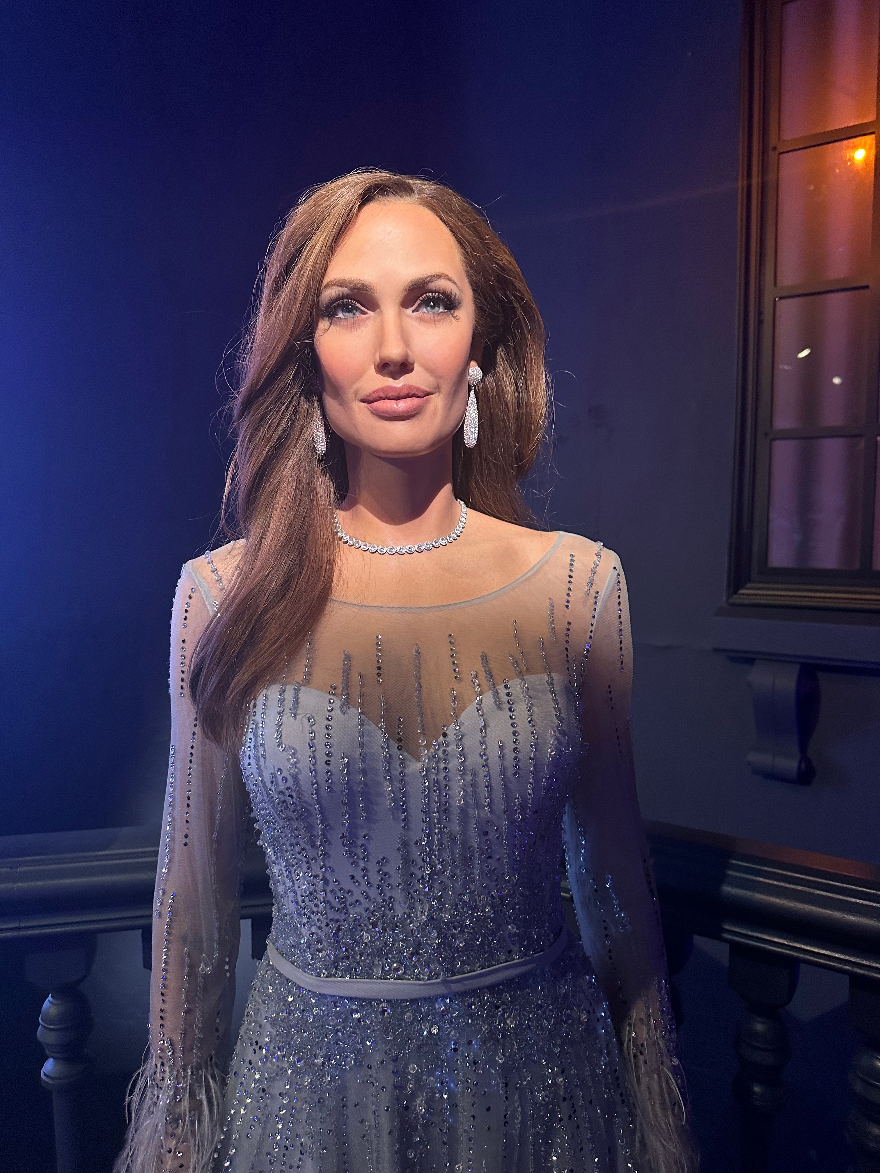 A figure in an elegant, beaded dress and jewelry poses in a glossy, indoor setting, relevant to travel news content