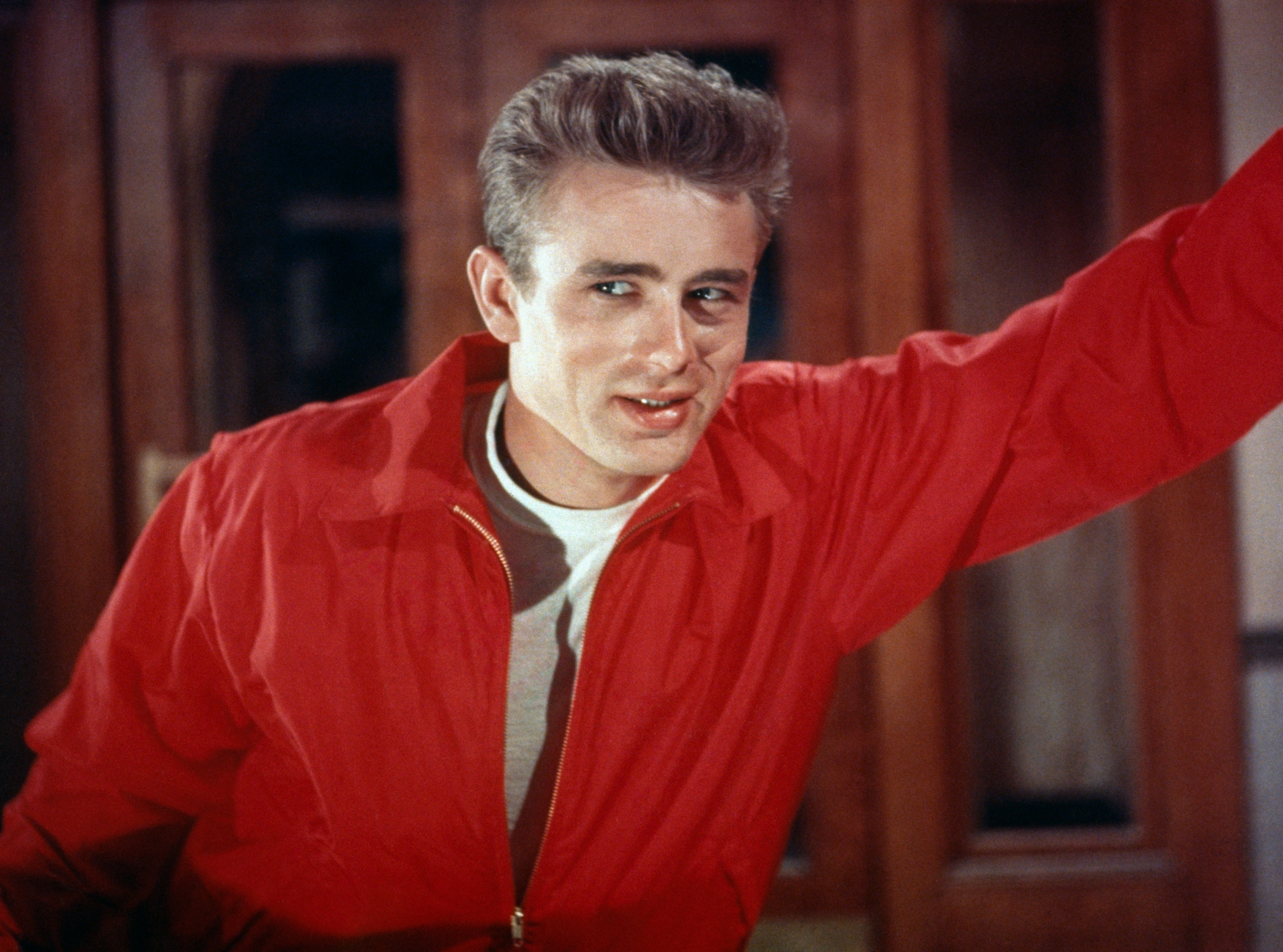 Person wearing a casual, open red jacket over a white T-shirt, smiling with relaxed demeanor indoors