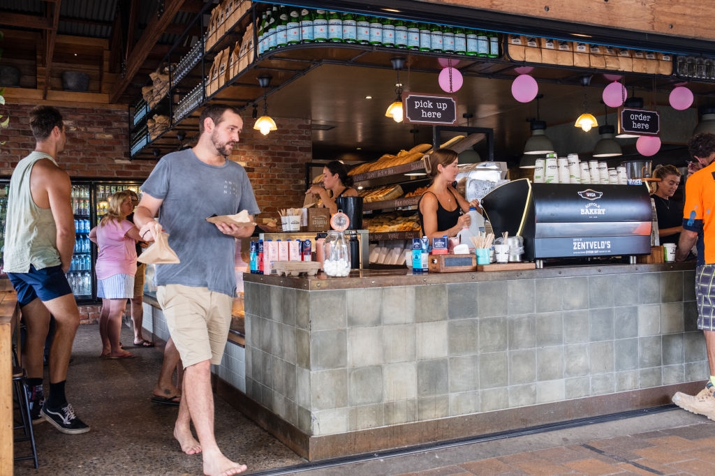 People at a busy café counter; one person in casual attire holds a food item while others are ordering and preparing coffee