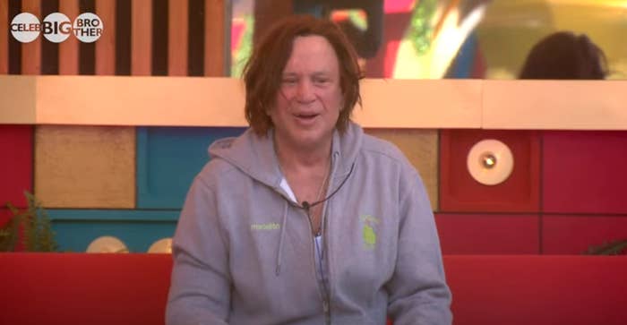 Person in a casual hoodie sits on a colorful couch on a set