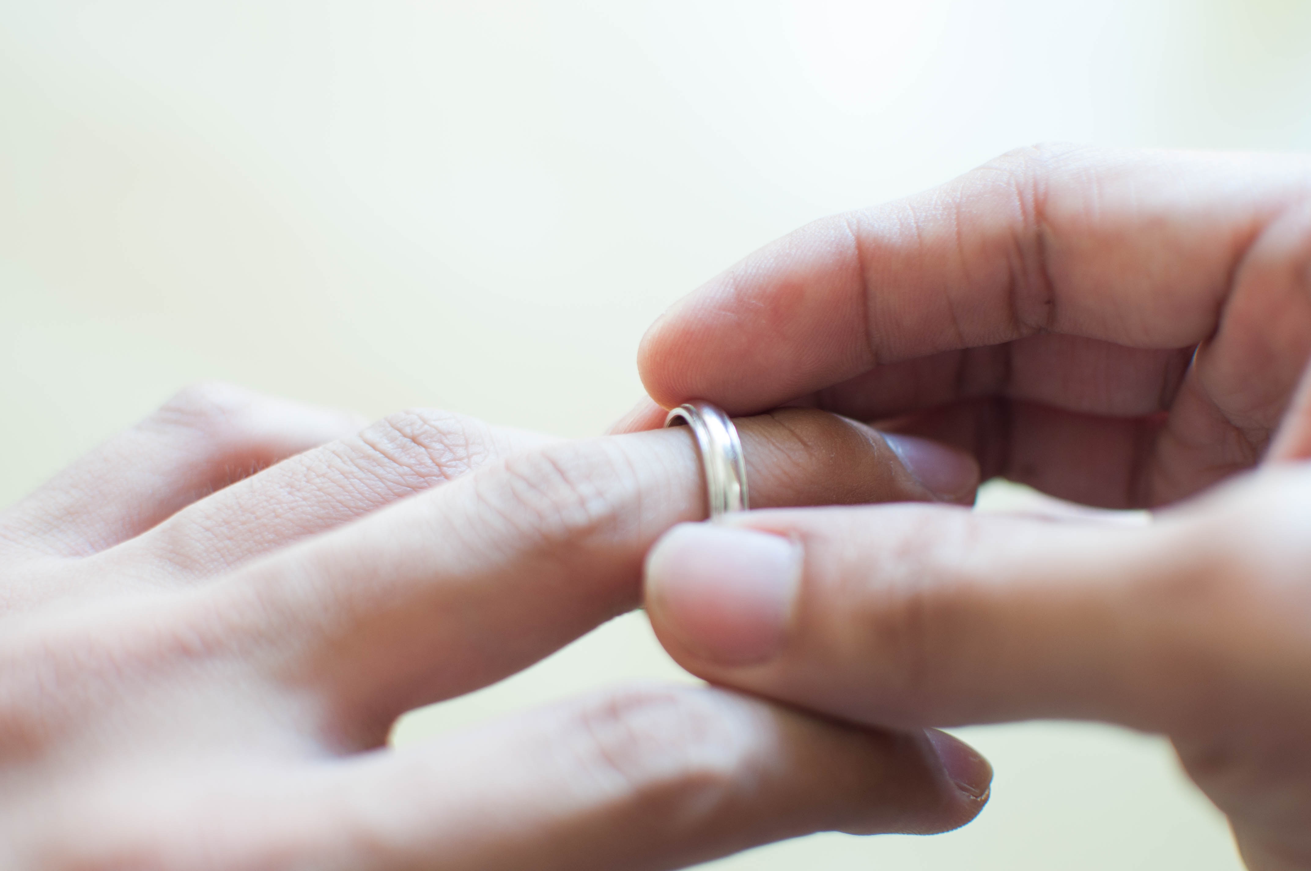A close-up of a hand placing a wedding ring on another person's finger, symbolizing love and commitment