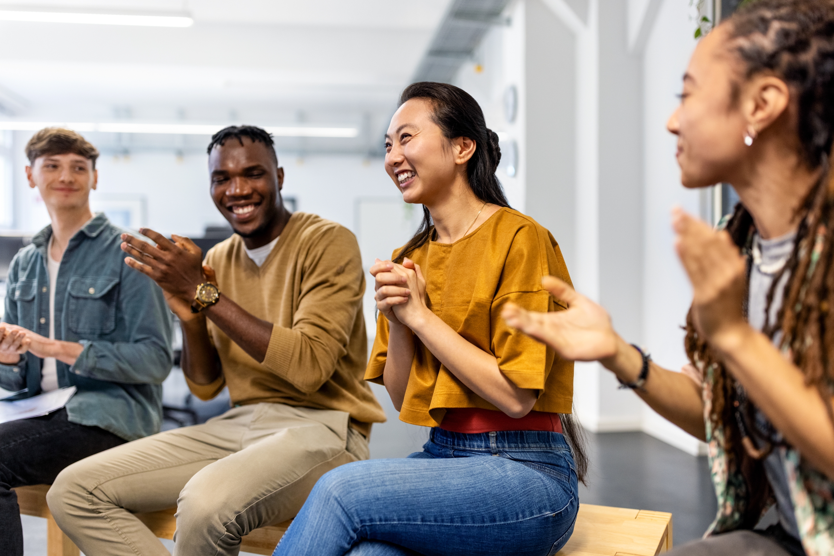 People sitting and clapping in a group discussion. Four individuals are engaged, smiling, and appear to be in a casual, friendly environment