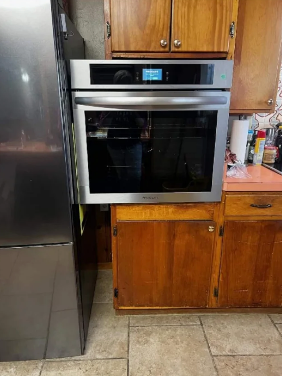Modern stainless steel oven poorly installed in wooden kitchen cabinetry — it's too big and fits oddly