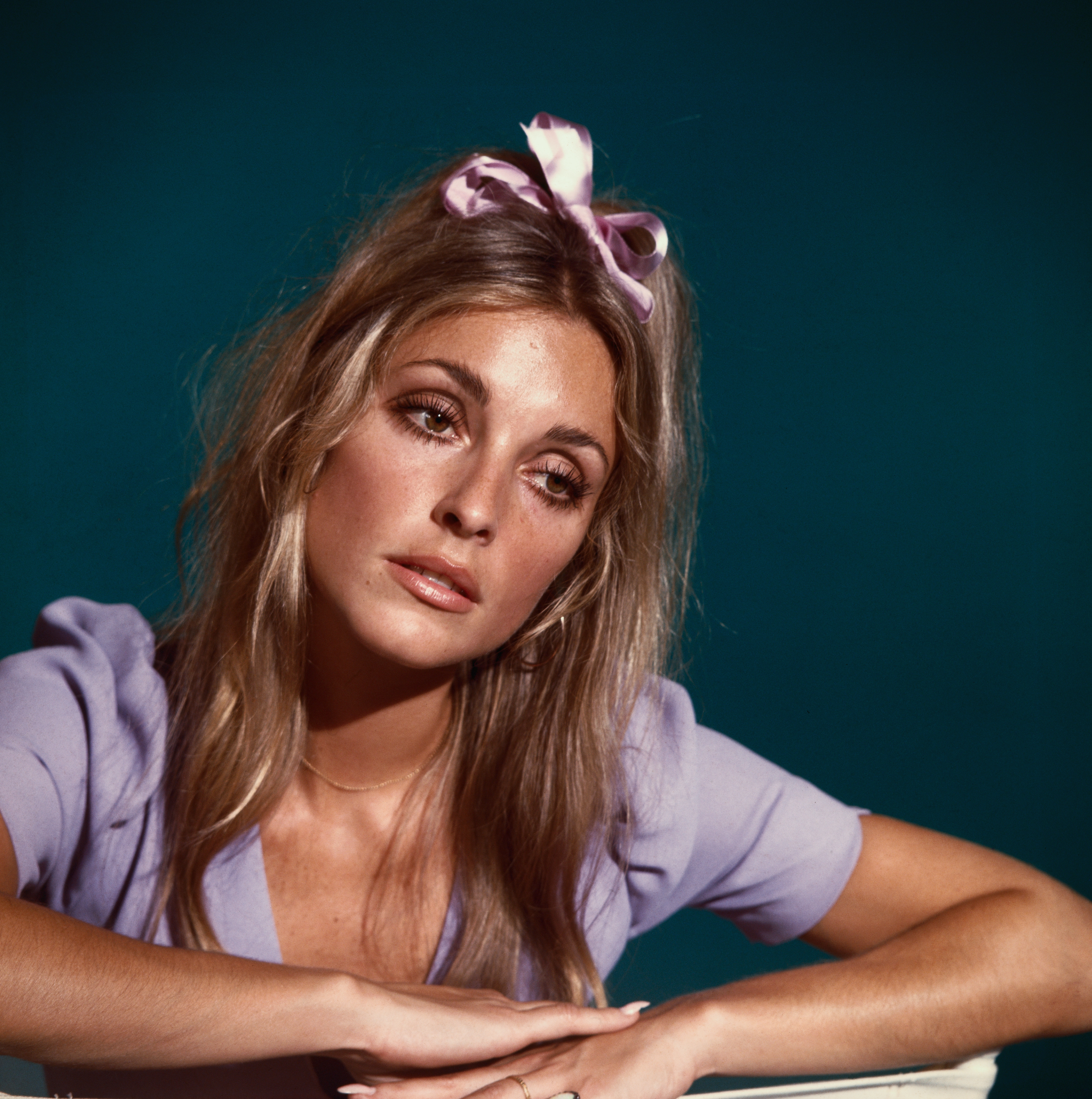 Person with long hair wearing a bow and light top, sitting with head slightly tilted, looking thoughtful
