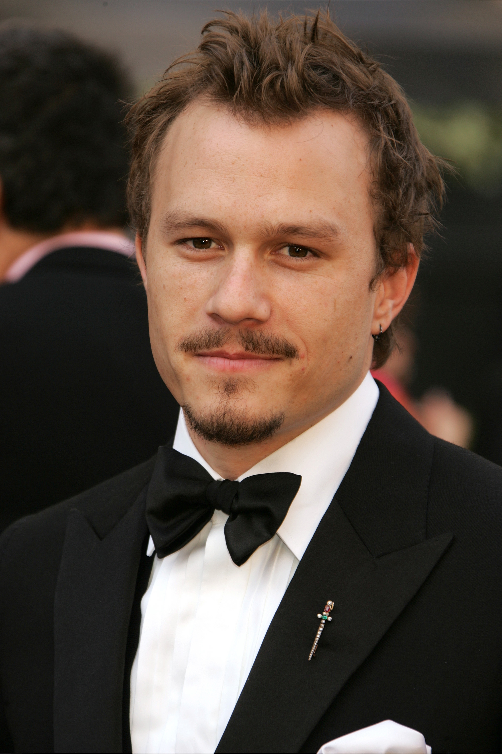 A person in formal attire with a bow tie smiles softly, with short wavy hair and a light goatee