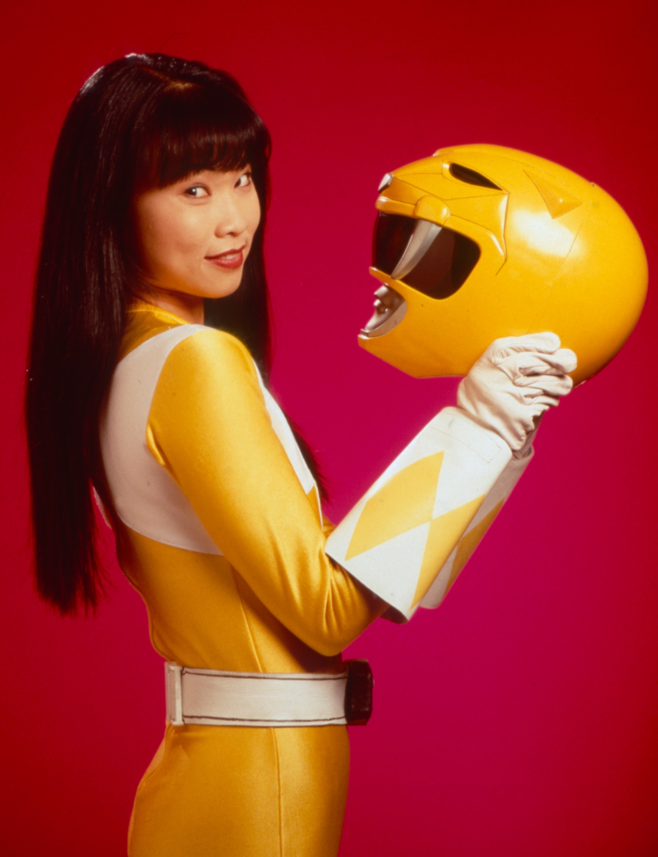 Person in Yellow Ranger suit holding matching helmet, facing sideways