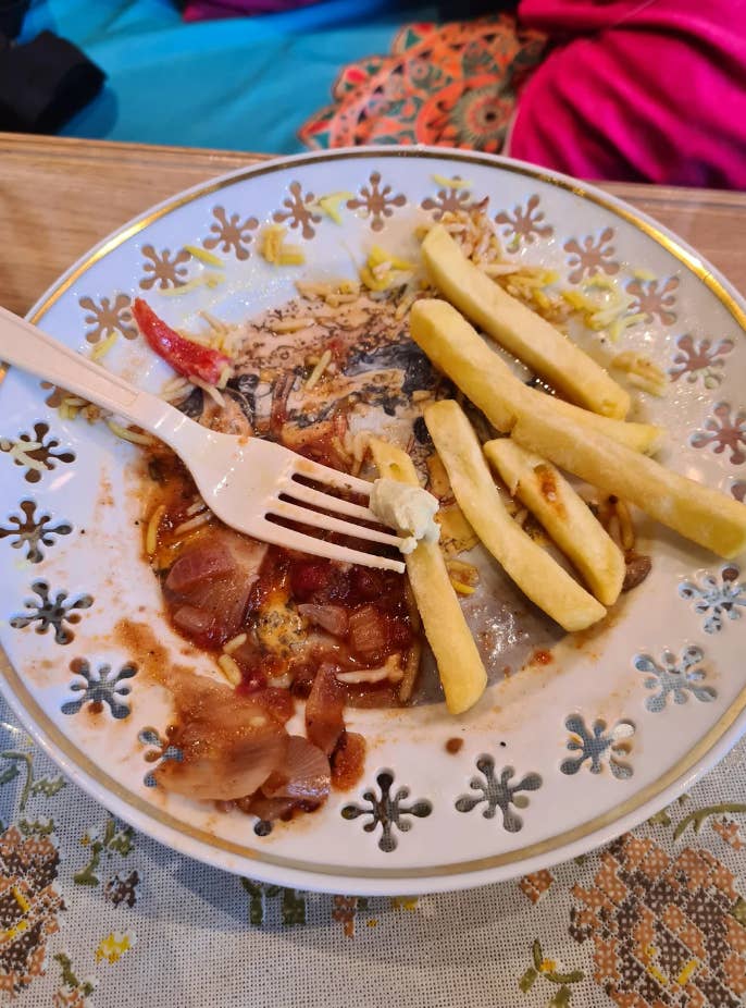 Plate with french fries, a fork, and remnants of a meal, including sauce and vegetables