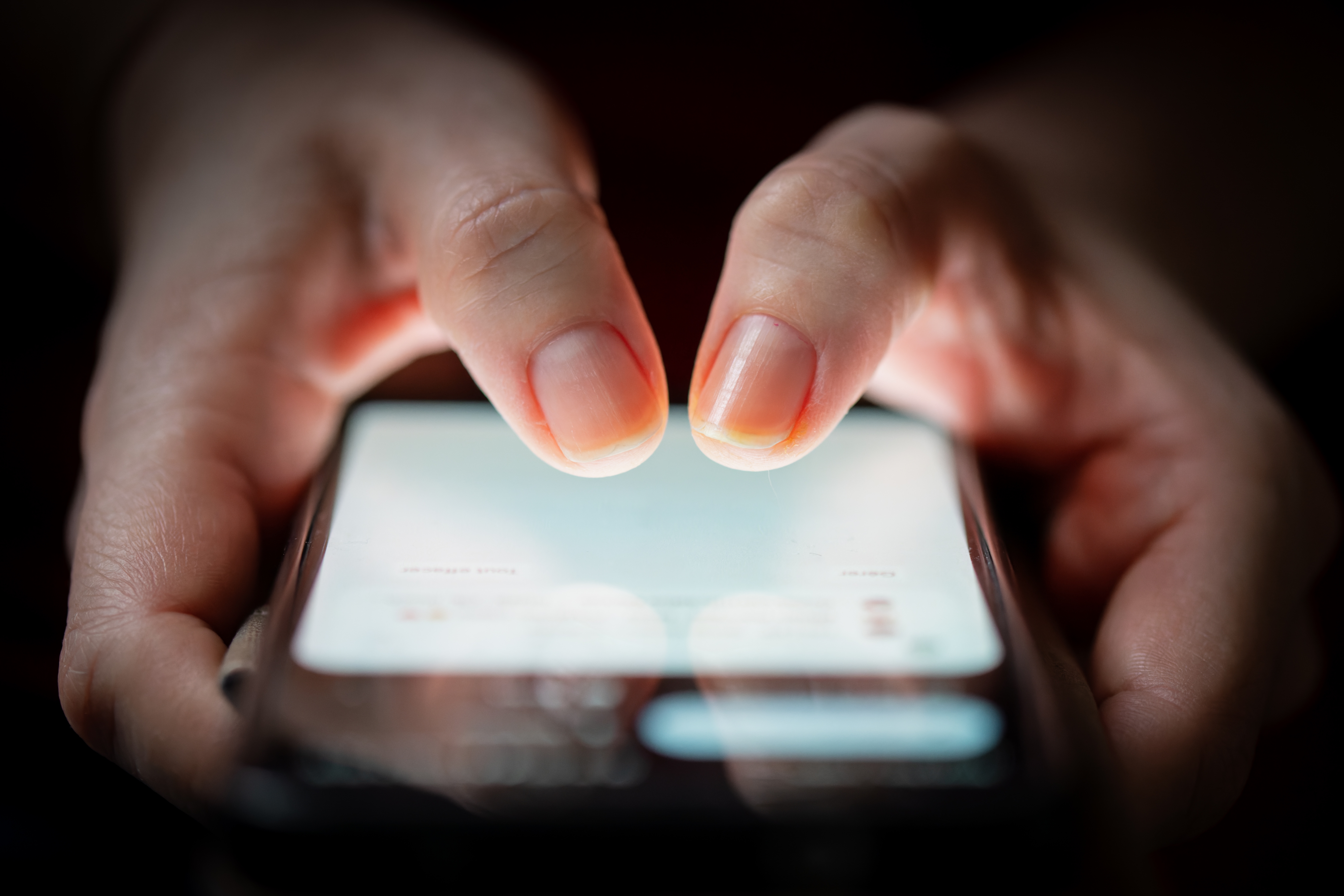 Fingre som skriver på en smarttelefonskjerm i en svakt opplyst setting, med fokus på den opplyste skjermen og personens hender