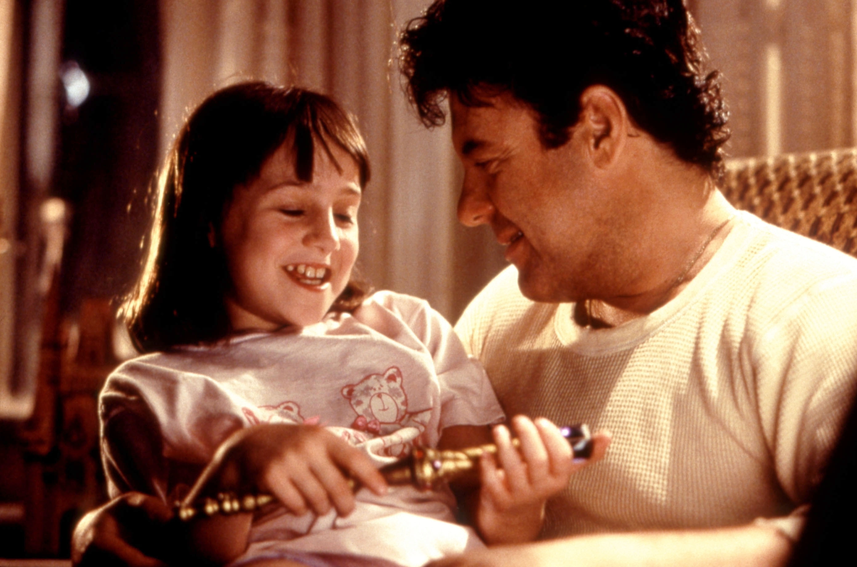 A man and a young girl are smiling at each other while holding a book, creating a warm and joyful moment