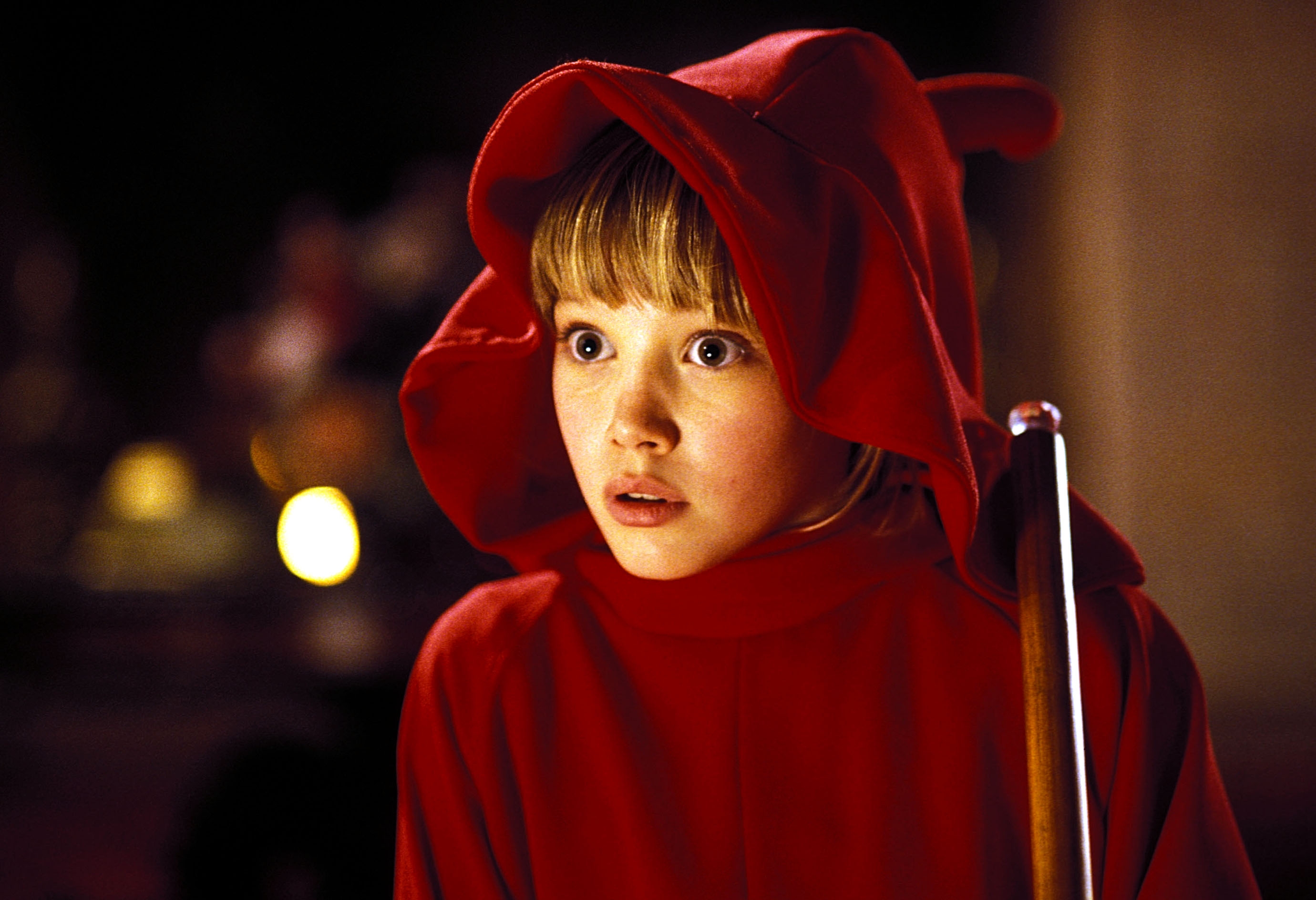 A young person in a red hooded cloak looks surprised, holding a pool cue