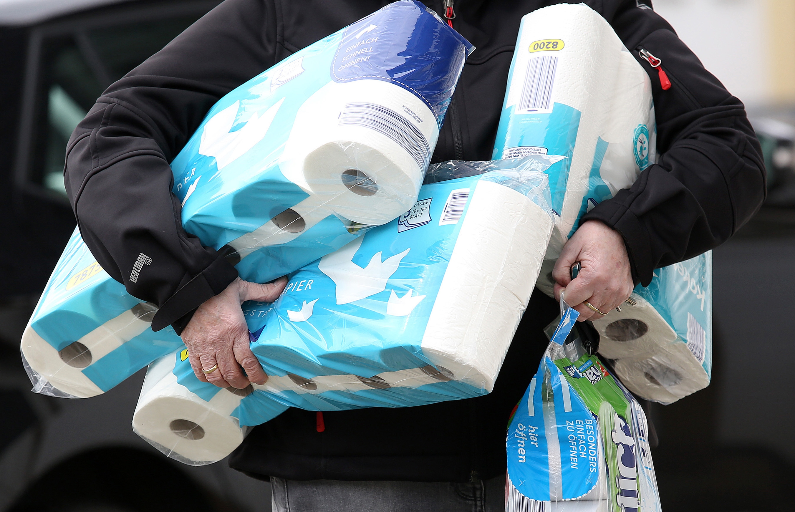 Person holding multiple packs of toilet paper, struggling to carry them all
