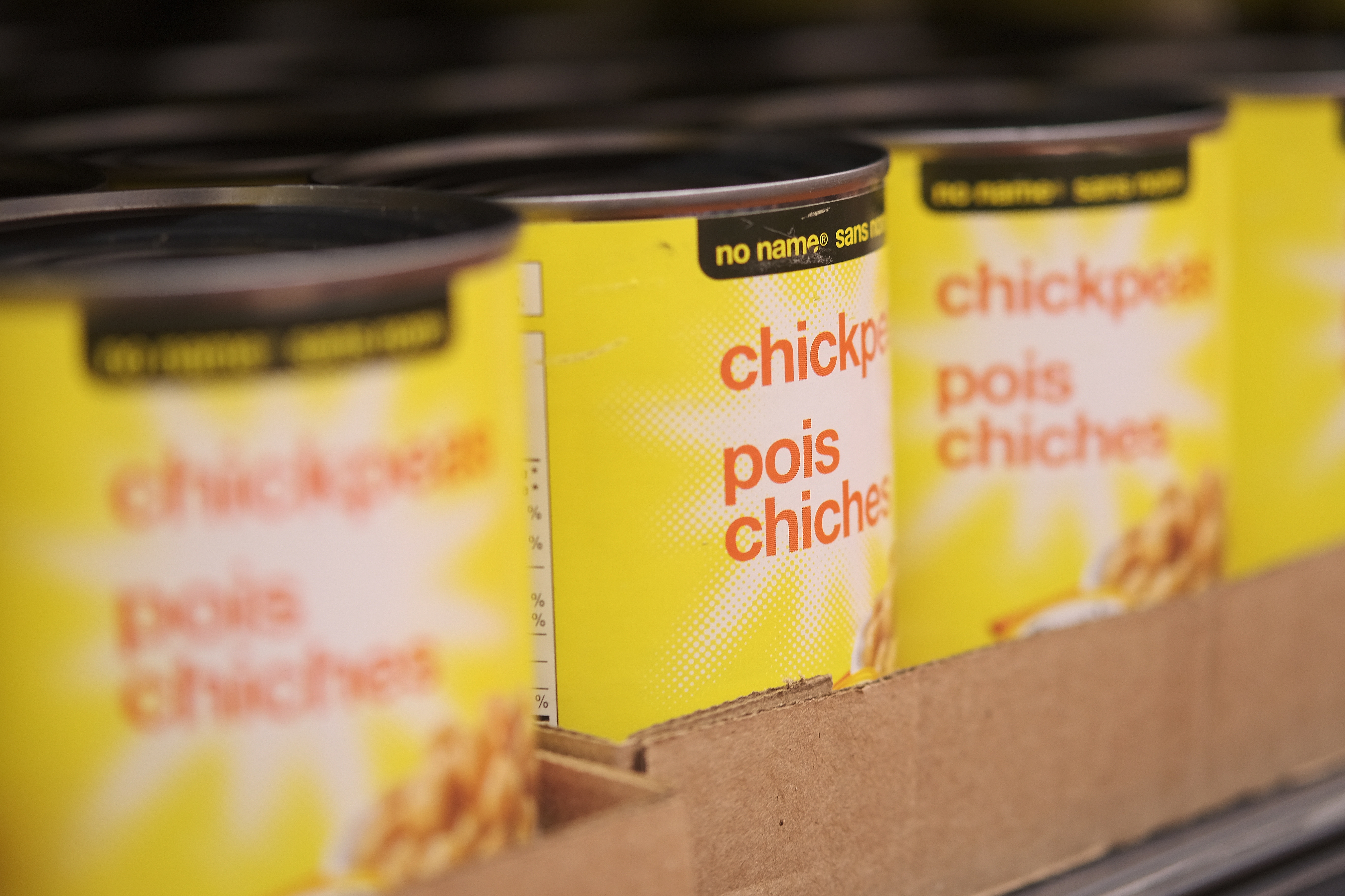 Cans of chickpeas stacked on a shelf, labeled in both English and French, in a cardboard box