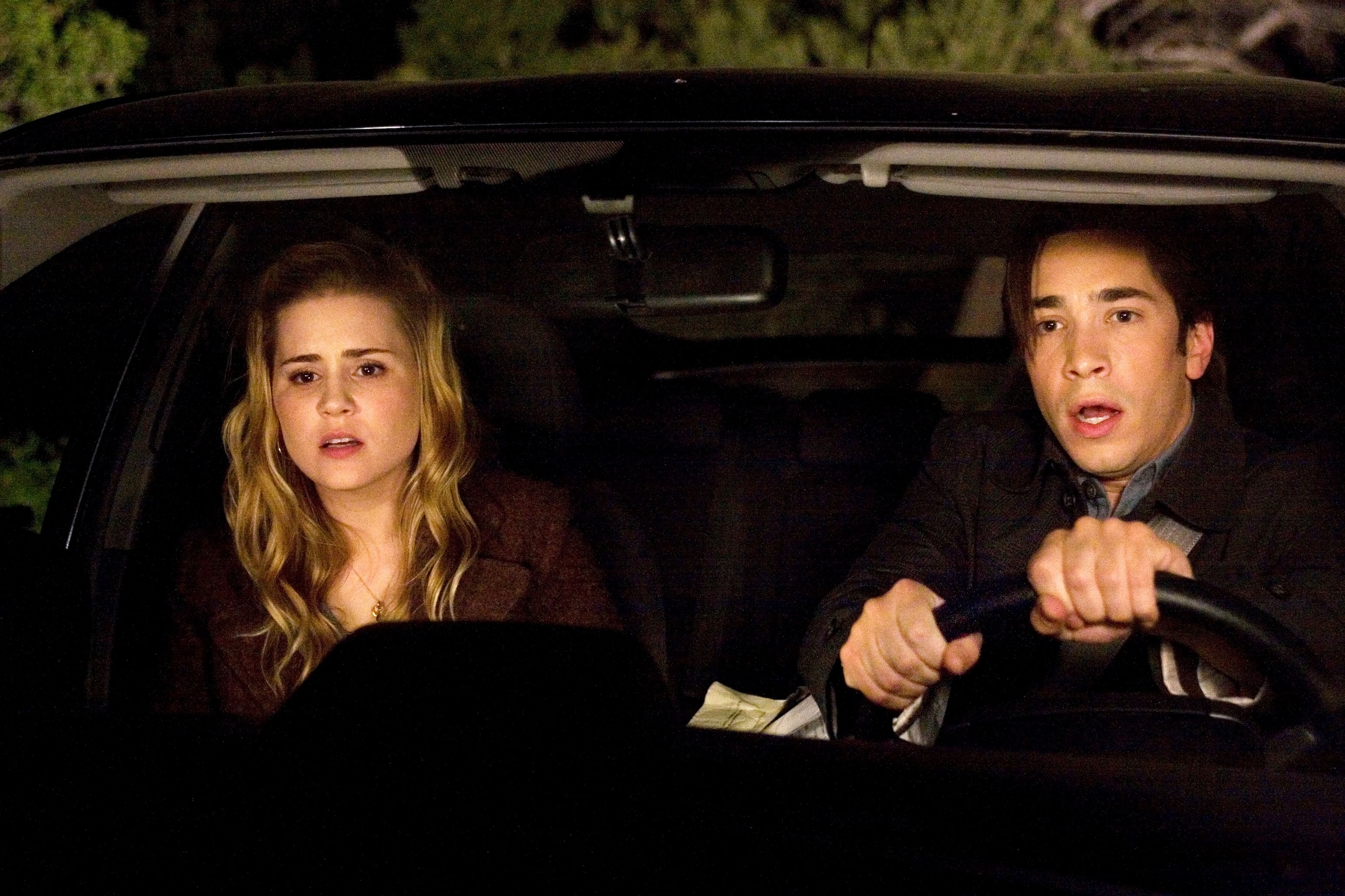 A young couple is in a car, appearing tense and focused