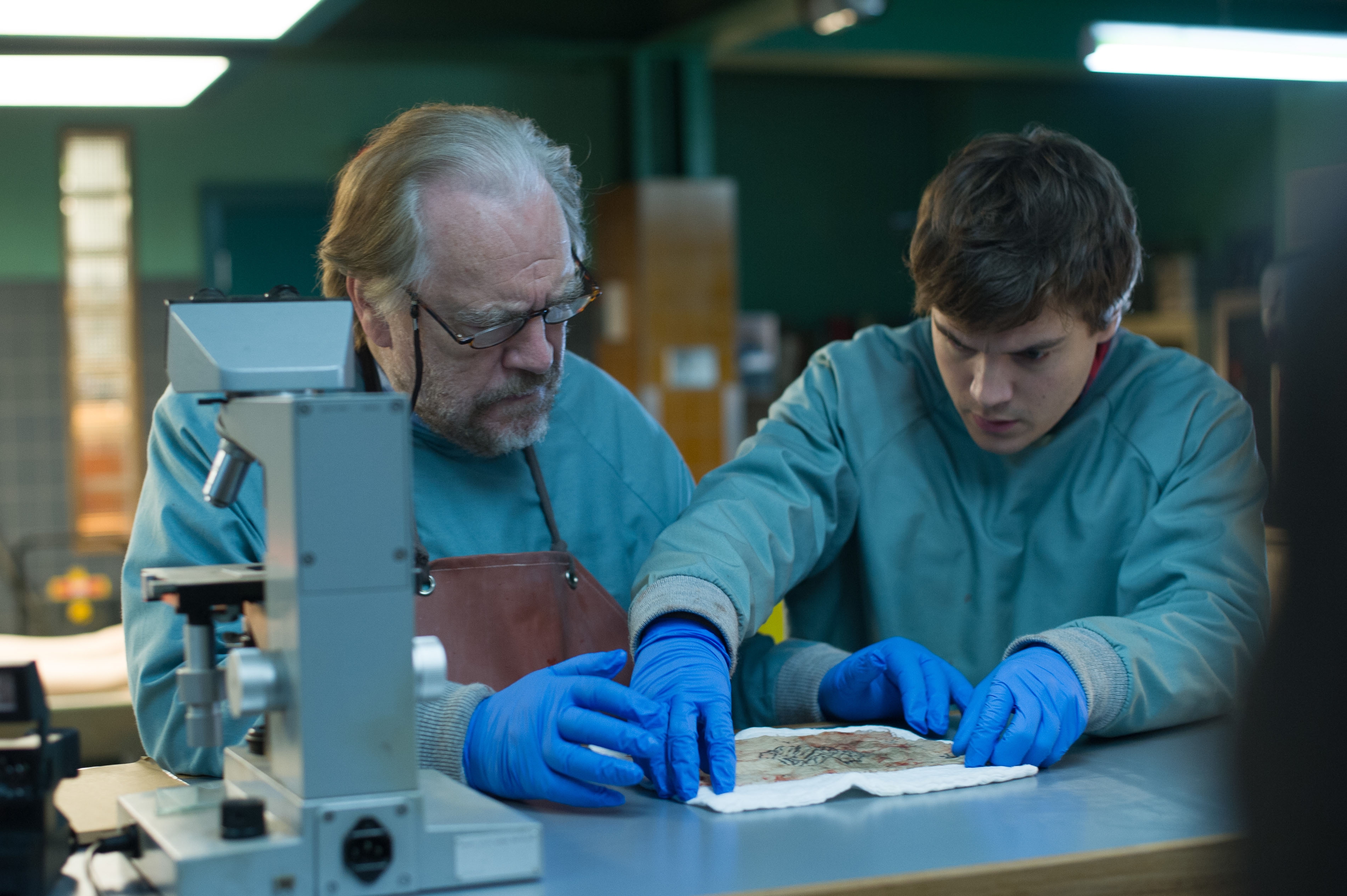 Two coroners in lab coats and gloves examine a document in a laboratory setting, with a microscope nearby