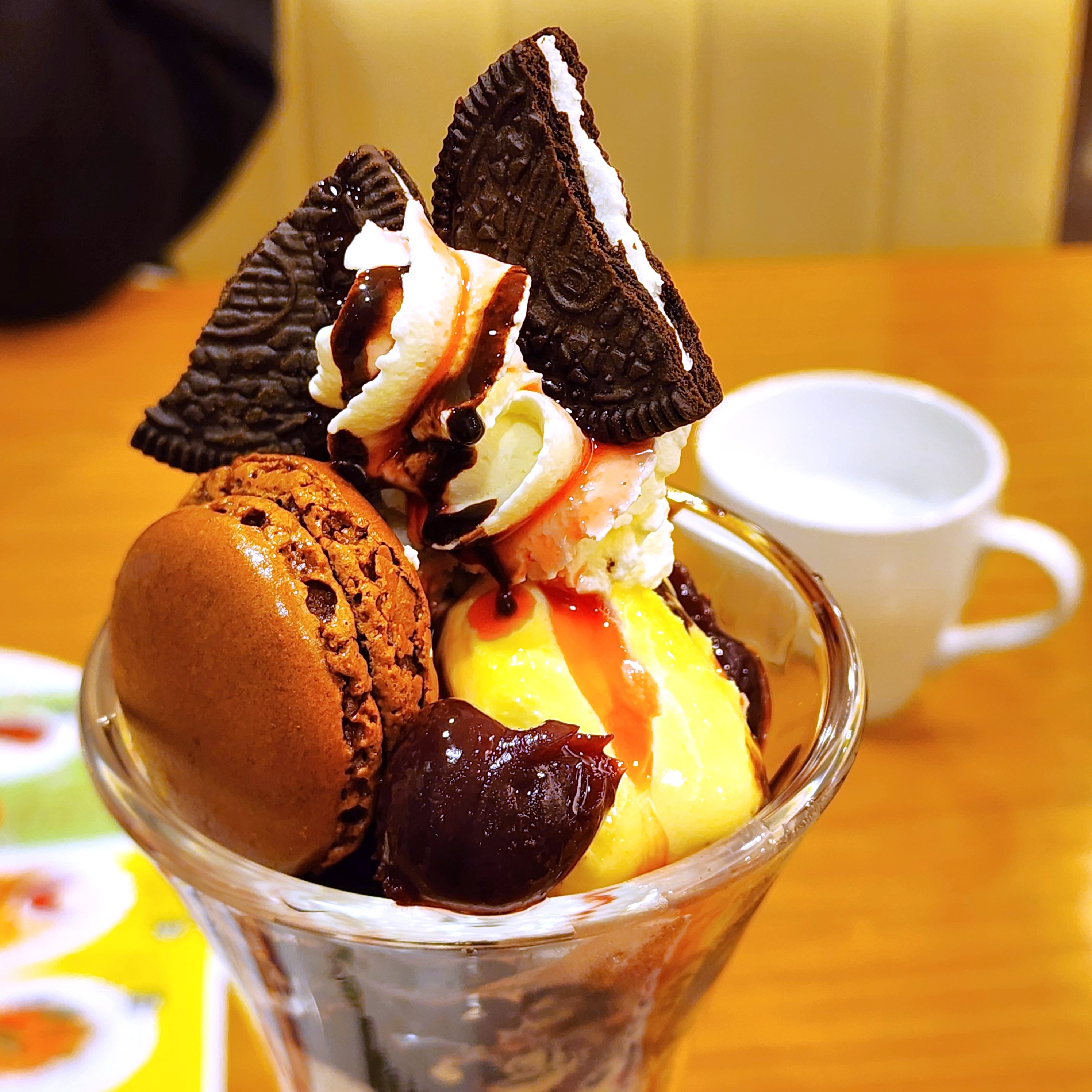クリーム、オレオクッキー、マカロンがトッピングされたアイスクリームパフェ。背景に白いカップが見える。