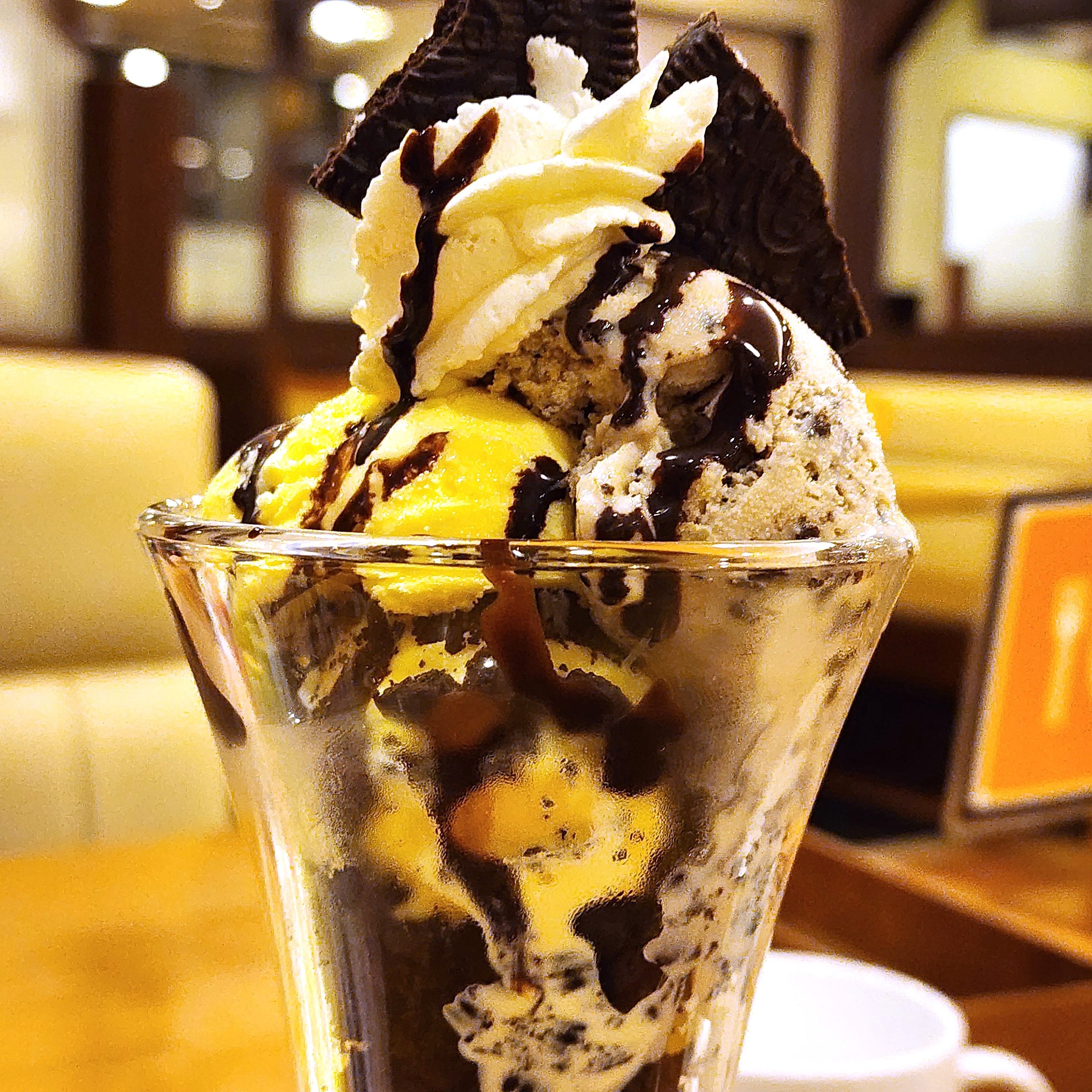 アイスクリームパフェがグラスに盛られ、チョコレートソースとクッキーがトッピングされています。