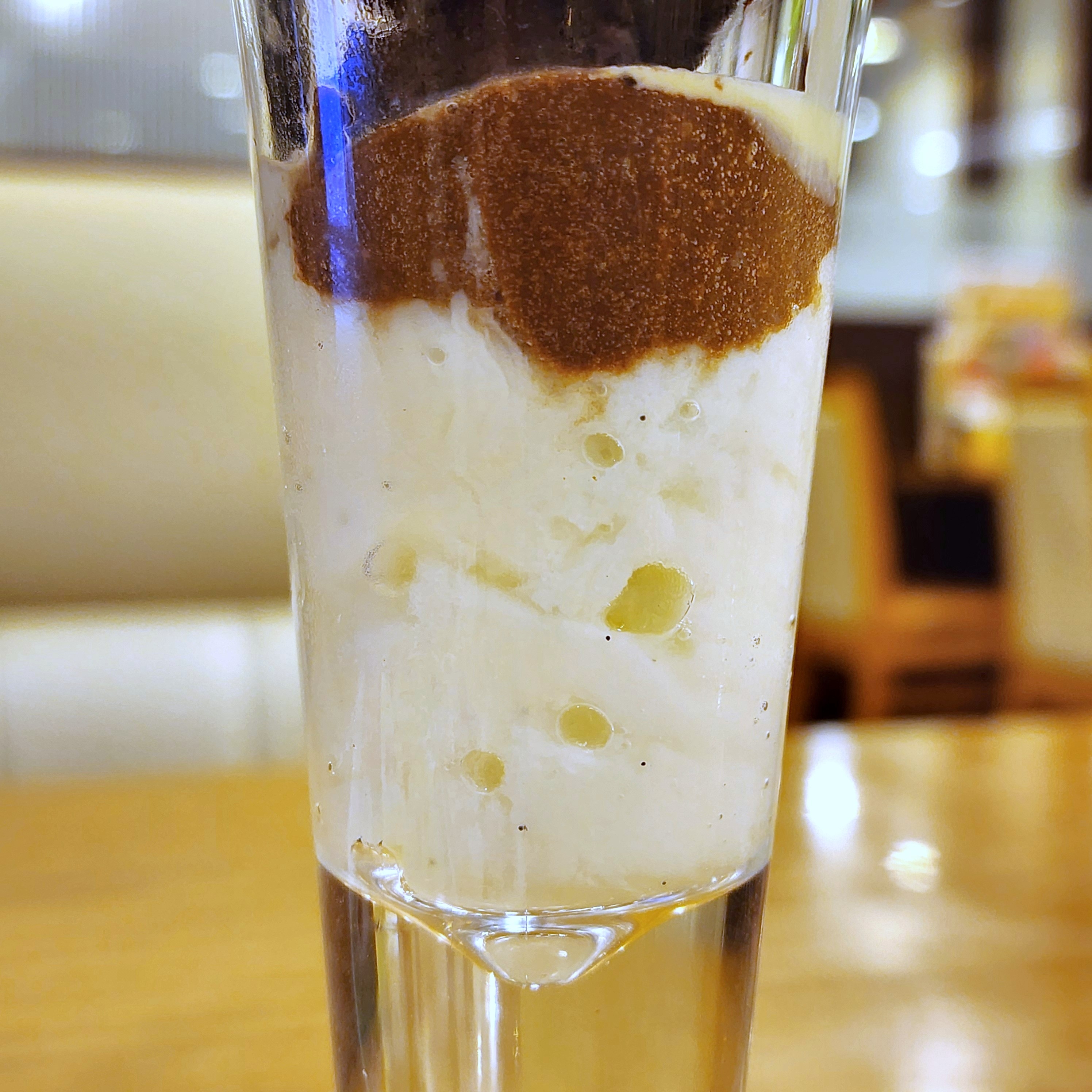 デザートグラスに盛られた、クリーミーなアイスクリームと泡立てたコーヒーのパフェ。カフェのテーブルに置かれている。