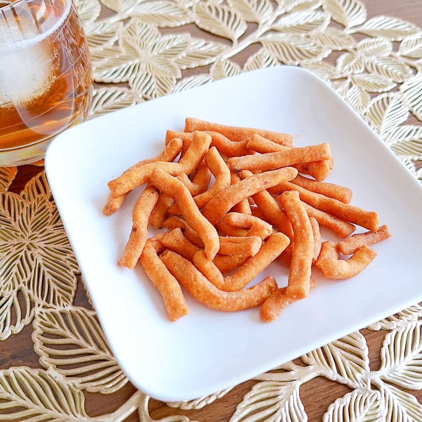 白い皿に盛られたスナック菓子と飲み物のカップ。パターンのあるテーブルクロスの上に置かれている。