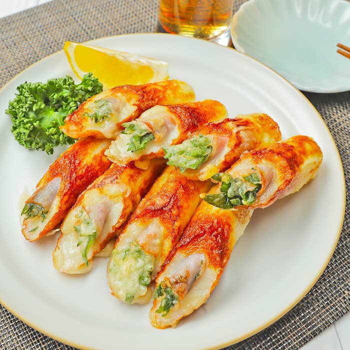 皿に盛られた数本の焼き魚練り物、レモン、パセリの添え物があります。背景に飲み物が見えます。