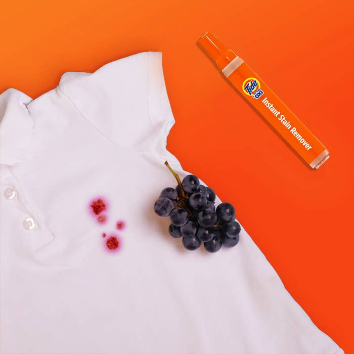 White garment  with grape foodstuff  stain adjacent  to a Tide Instant Stain Remover pen and grapes
