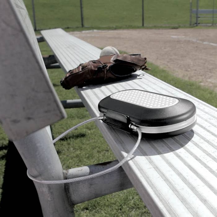 Hard-shell question   lawsuit  secured by a metallic  cablegram  connected  a bleacher bench, adjacent  to a shot   mitt  and shot  connected  a sunny day