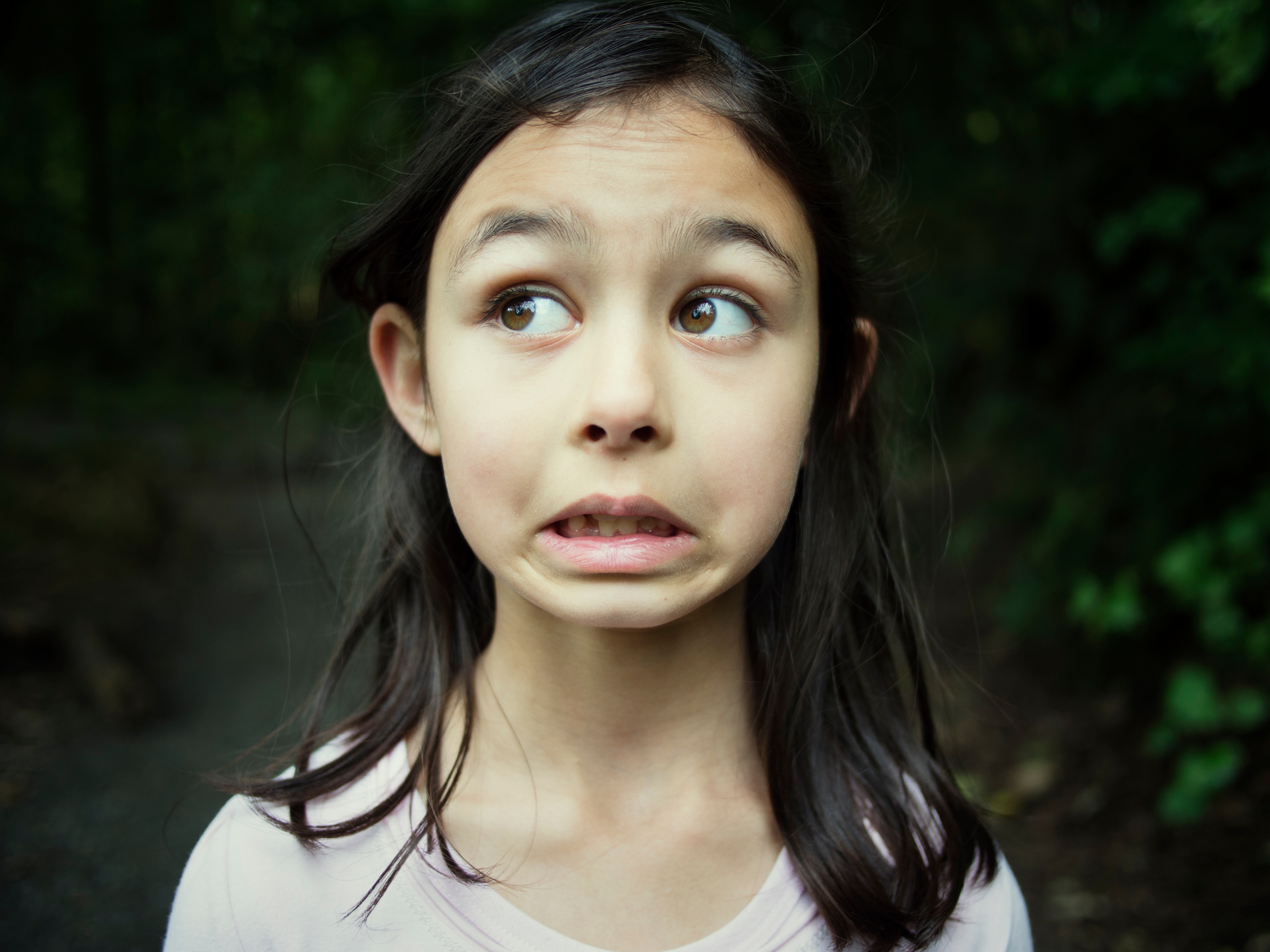 Young girl with long hair looks sideways with a humorous expression in an outdoor setting