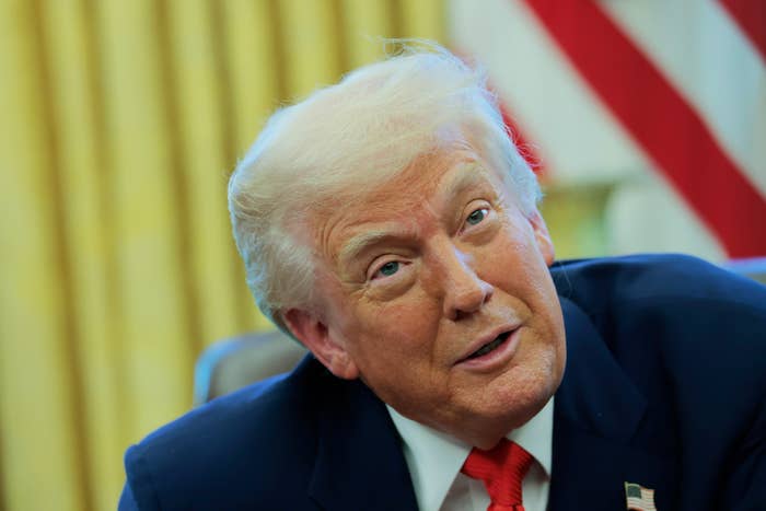 President Donald Trump in a suit and red tie, seated in the Oval Office