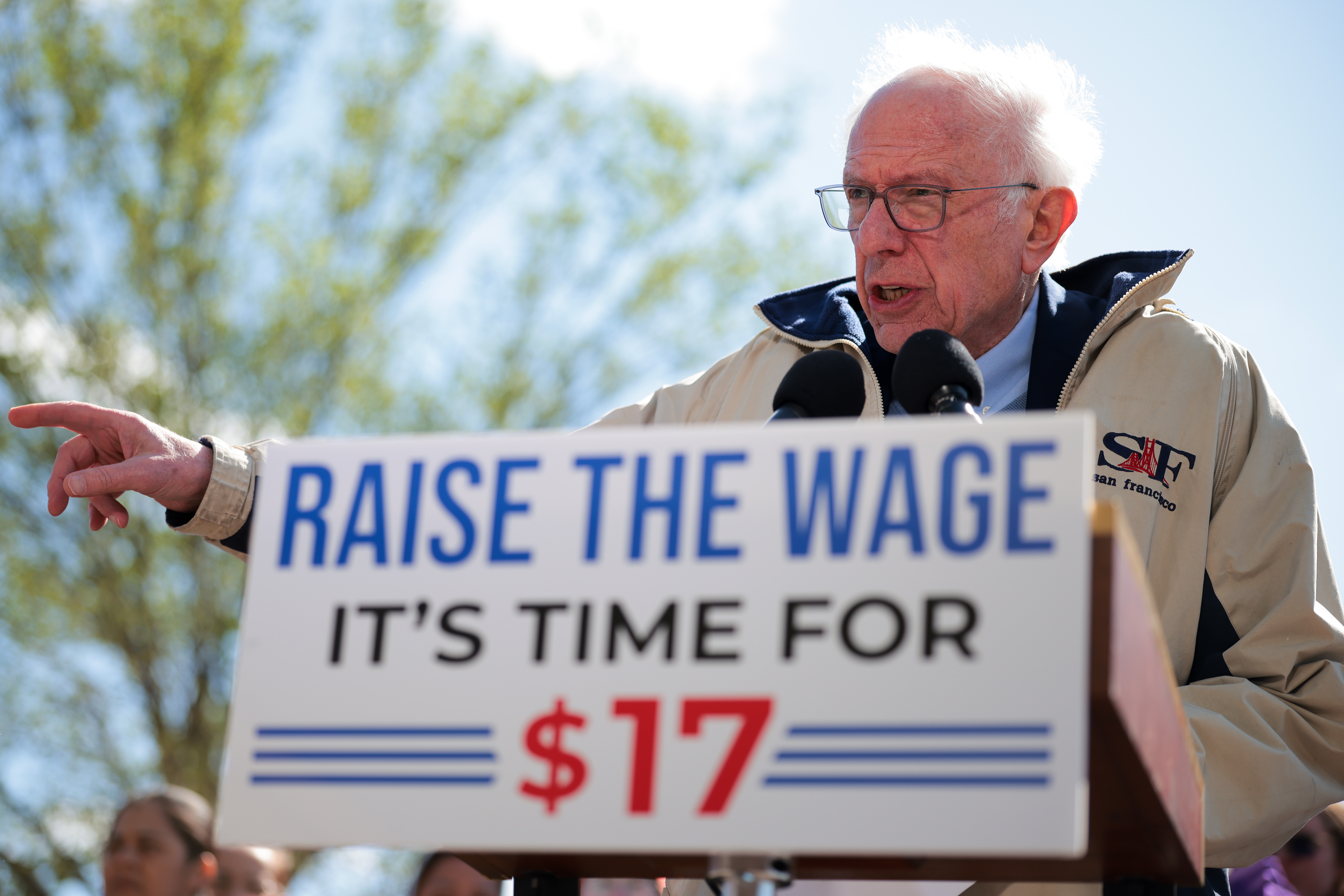 Senator Bernie Sanders speaking at a podium with a sign reading "Raise the Wage. It's Time for $17," emphasizing wage increase advocacy