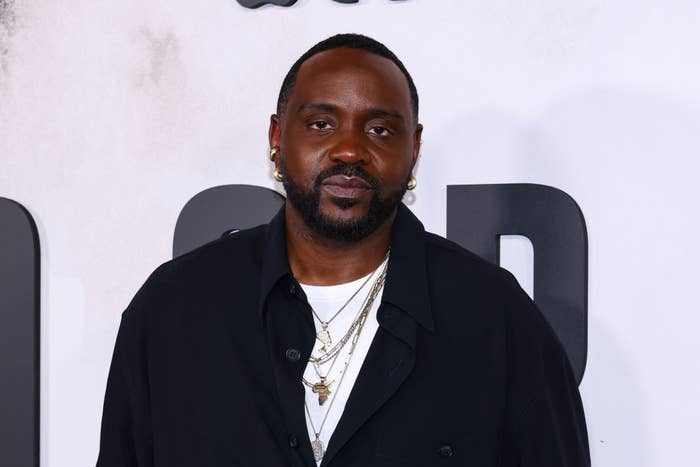 Person wearing a black jacket with layered gold necklaces at a media event