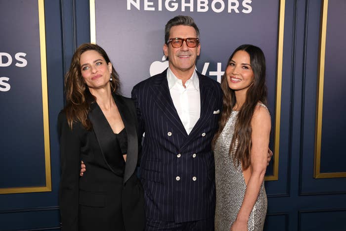 Amanda Peet, Jon Hamm, and Olivia Munn pose together at an event. One person wears a suit, while the others wear stylish evening attire