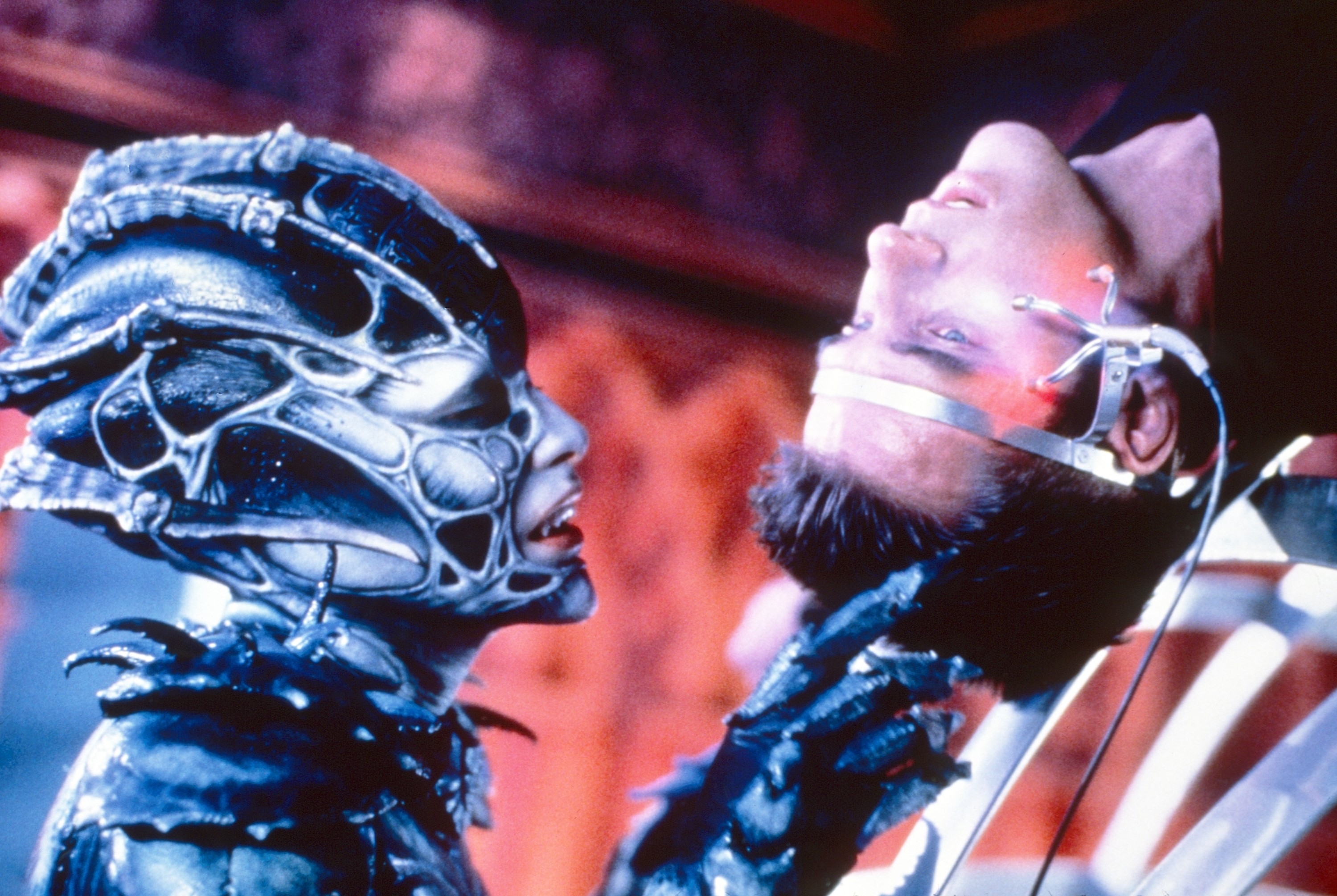 A character in futuristic armor interacts with another character in a mechanical headpiece,