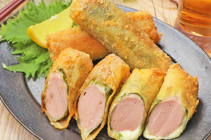 春巻きに似た料理が皿に盛られている。ソーセージとチーズが入っており、レモンスライスと葉が添えられている。