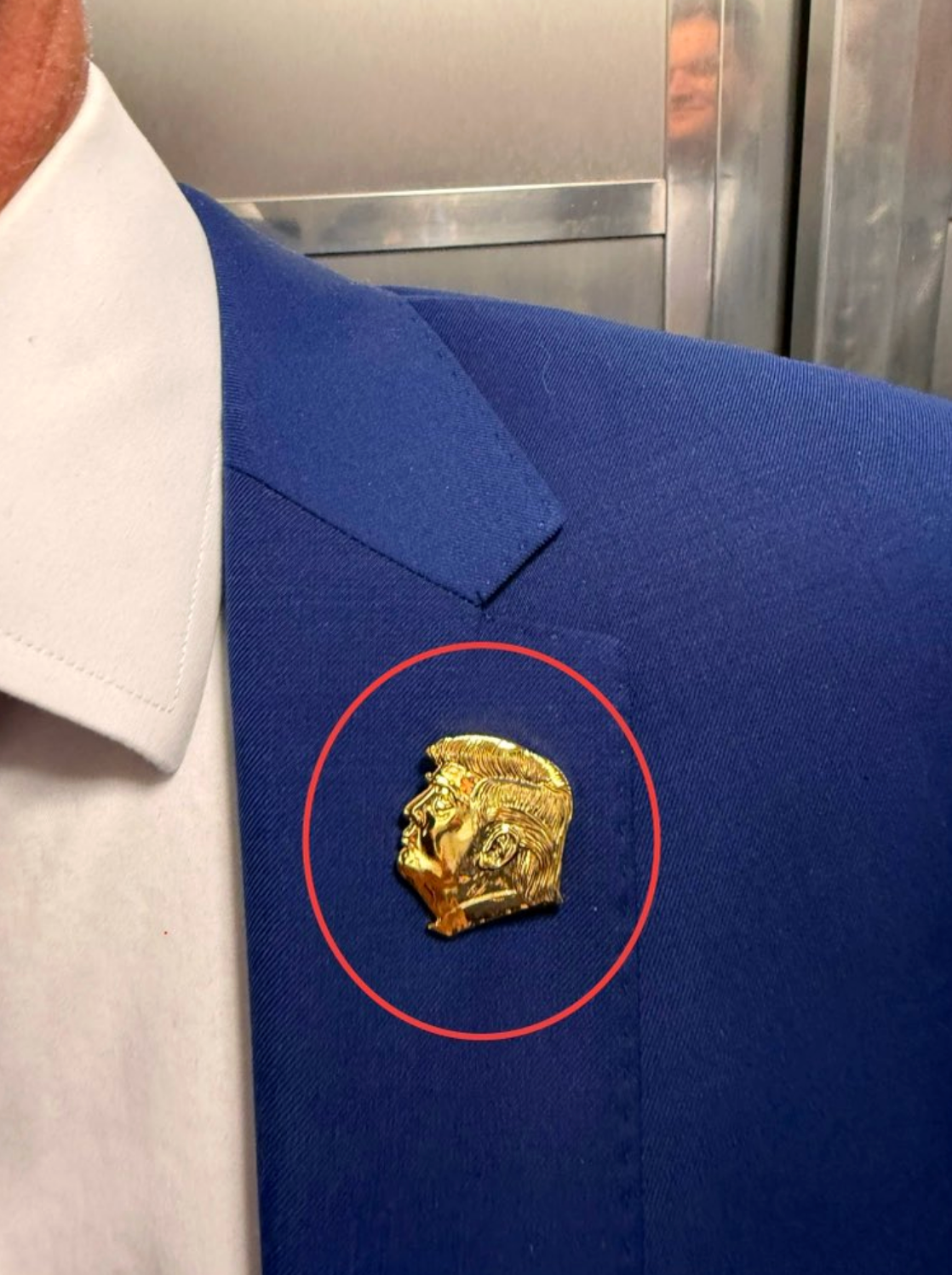 A gold pin resembling Trump's face is attached to the lapel of a blue suit jacket