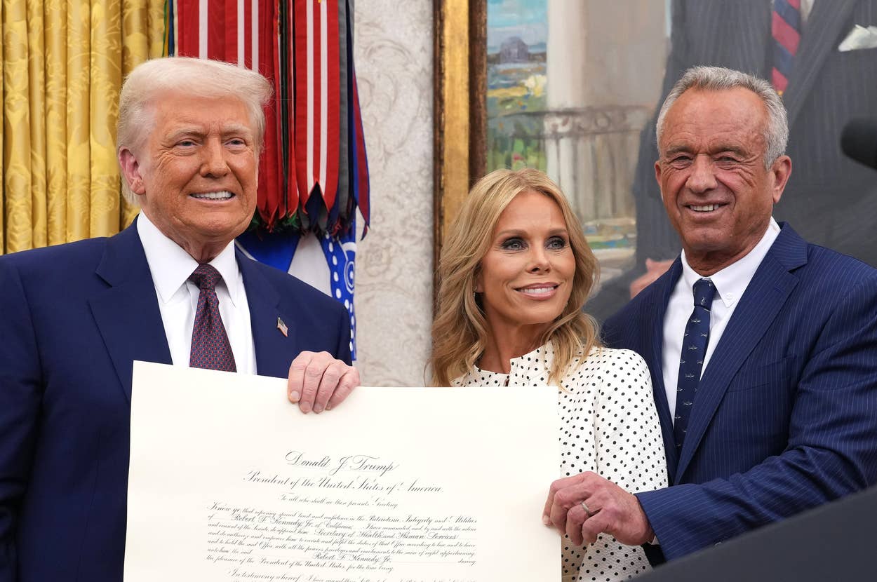 Three people stand in a formal setting holding a large certificate, smiling at the camera