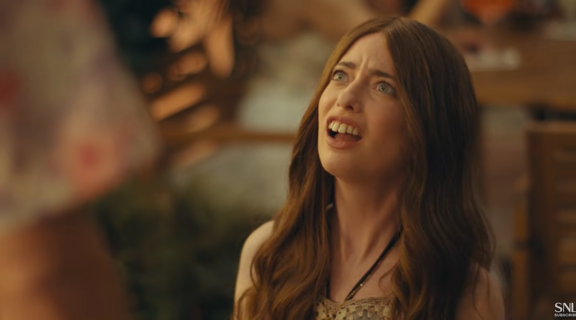 Sarah Sherman with long hair looks up, mouth open. Casual indoor setting in the background